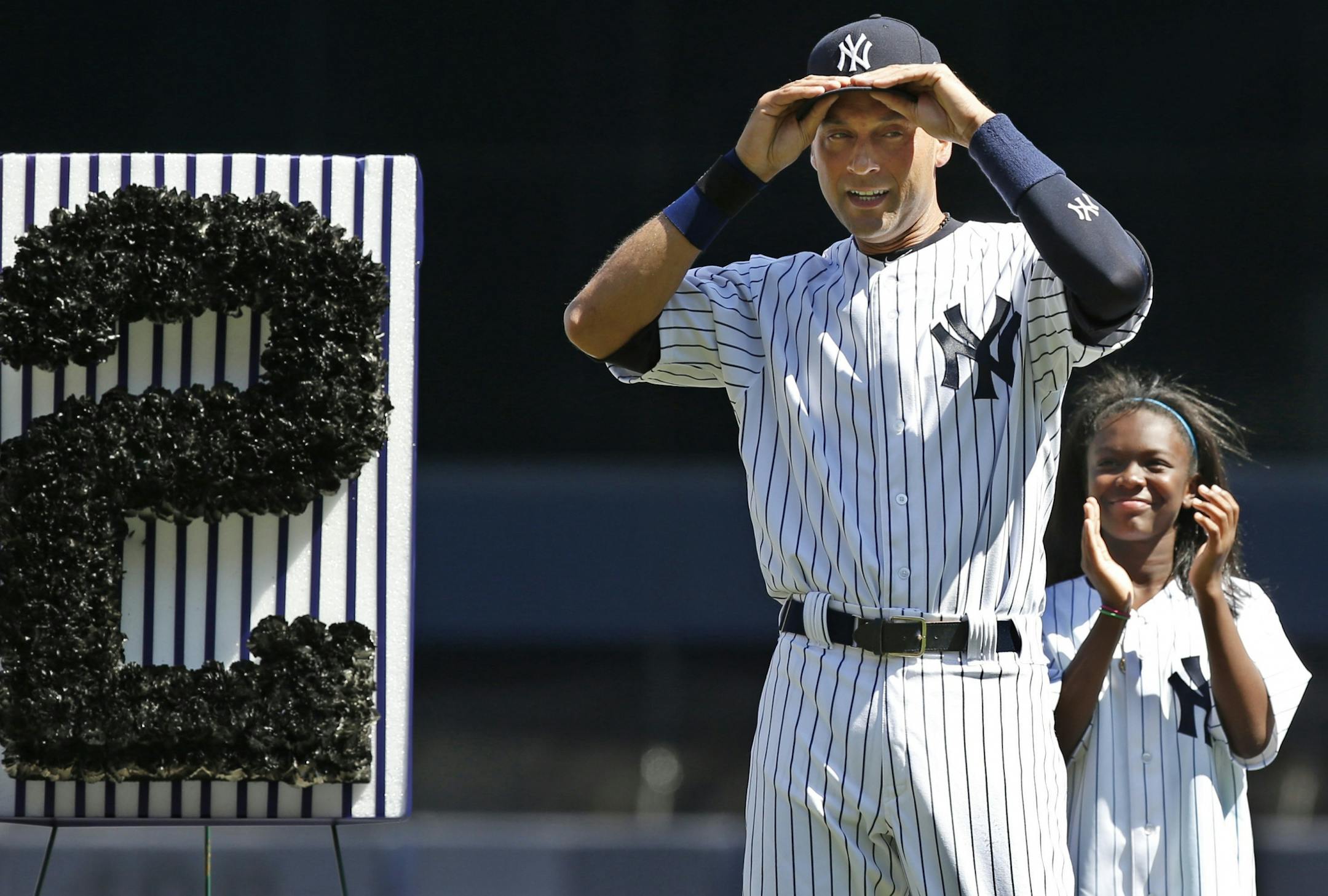 A youngster applauds as New York Yankees shortstop Derek Jeter (2) adjusts his cap after tipping it to the crowd during a pregame ceremony honoring the Yankees captain who is retiring at the end of the season on Derek Jeter Day at Yankee Stadium in New York, Sunday, Sept. 7, 2014.