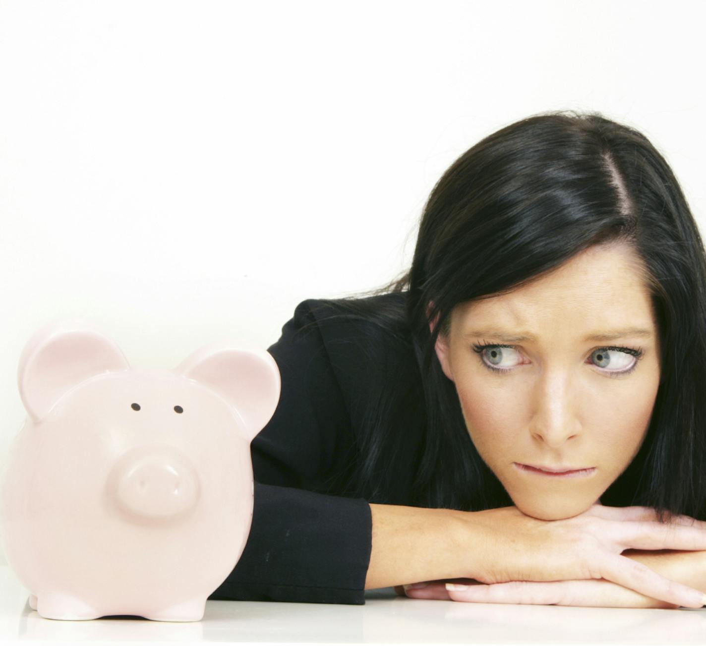 A woman looks worriedly at her piggy bank