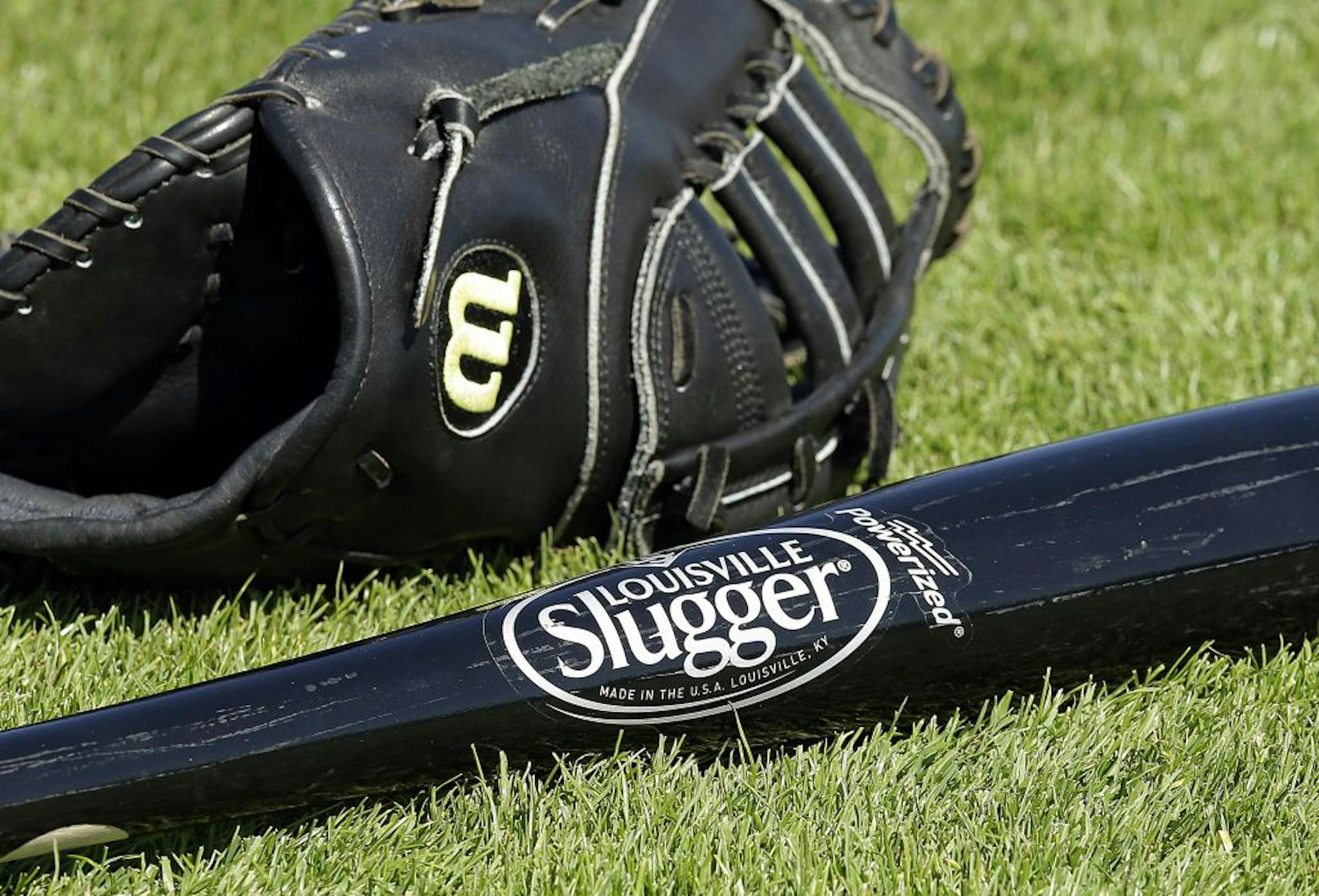 A Wilson baseball glove and a Louisville slugger bat sit on the field prior to a spring training baseball game between the Kansas City Royals and the San Francisco Giants on Monday, March 23, 2015, in Scottsdale, Ariz. Hillerich & Bradsby Co., the company that made bats for a who's who of baseball greats, including Babe Ruth and Ted Williams, announced a deal Monday to sell its Louisville Slugger brand to rival Wilson Sporting Goods Co. for $70 million.