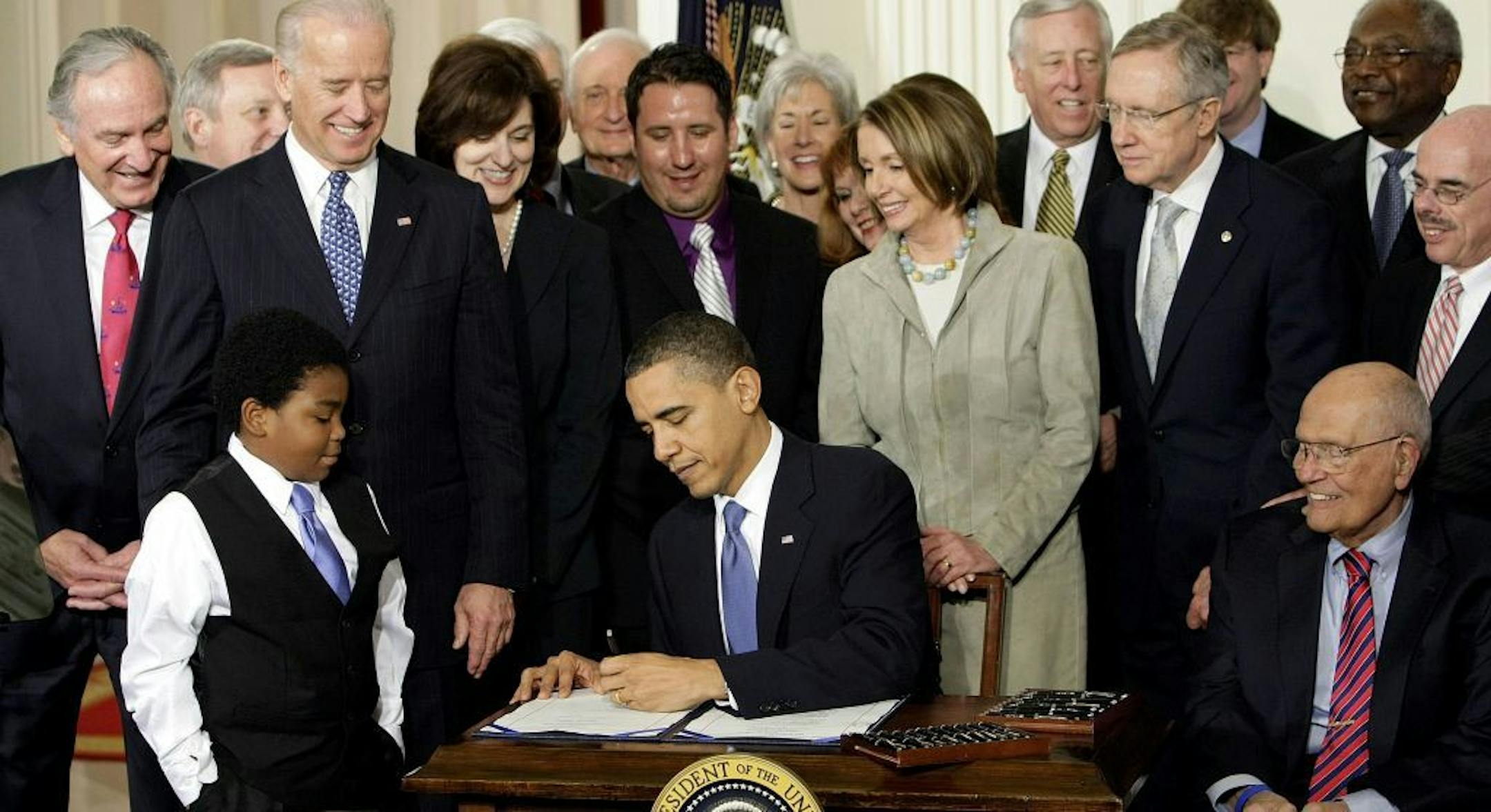 FILE - In this March 23, 2010 file photo, President Barack Obama signs the Affordable Care Act in the East Room of the White House in Washington. If Obama's health care law survives Supreme Court scrutiny, it will be nearly a decade before all its major pieces are in place. The law's carefully orchestrated phase-in is evidence of what's at stake in the Supreme Court deliberations that start March 26, 2012. With Obama are Marcelas Owens of Seattle, left, and Rep. John Dingell, D-Mich., right; fro
