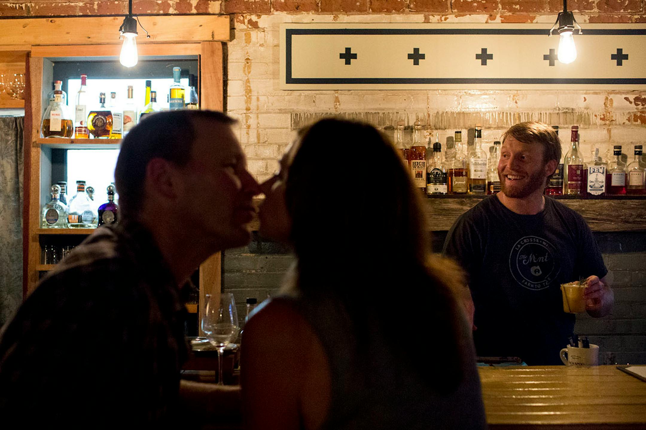 Joe and Tracy Endeizzi kiss at The Mint while Mathew Steers (right) makes drinks. ] COURTNEY PEDROZA • courtney.pedroza@startribune.com June 22-24, 2017; Wisconsin restaurants, cafes, bars, bakeries and breweries; Dining along the Mississippi River.
