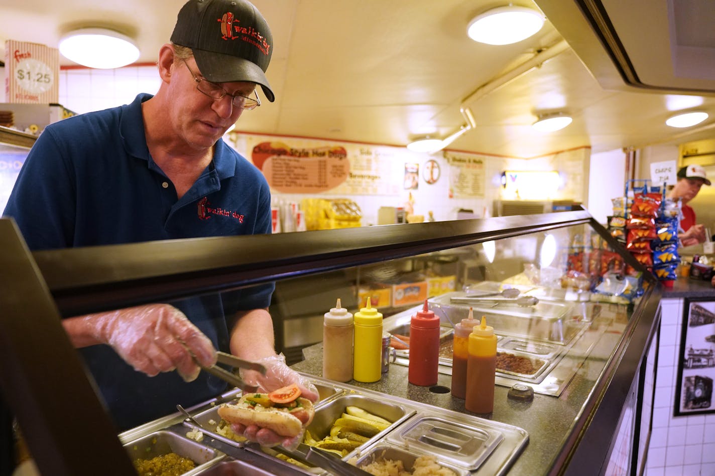 Dave Maguson served up a Chicago style hot dog at his Walkin' Dog stand. ] ANTHONY SOUFFLE &#x2022; anthony.souffle@startribune.com Dave Magnuson, proprietor of downtown's stalwart hot-dog stand, Walkin' Dog, served up lunch for customers Tuesday, April 23, 2019 in Minneapolis. Maguson has brought cheap eats and a small-town style to the skyway system for 28 years - eating 3.5 miles of franks and missing a mere four days of work in the process.