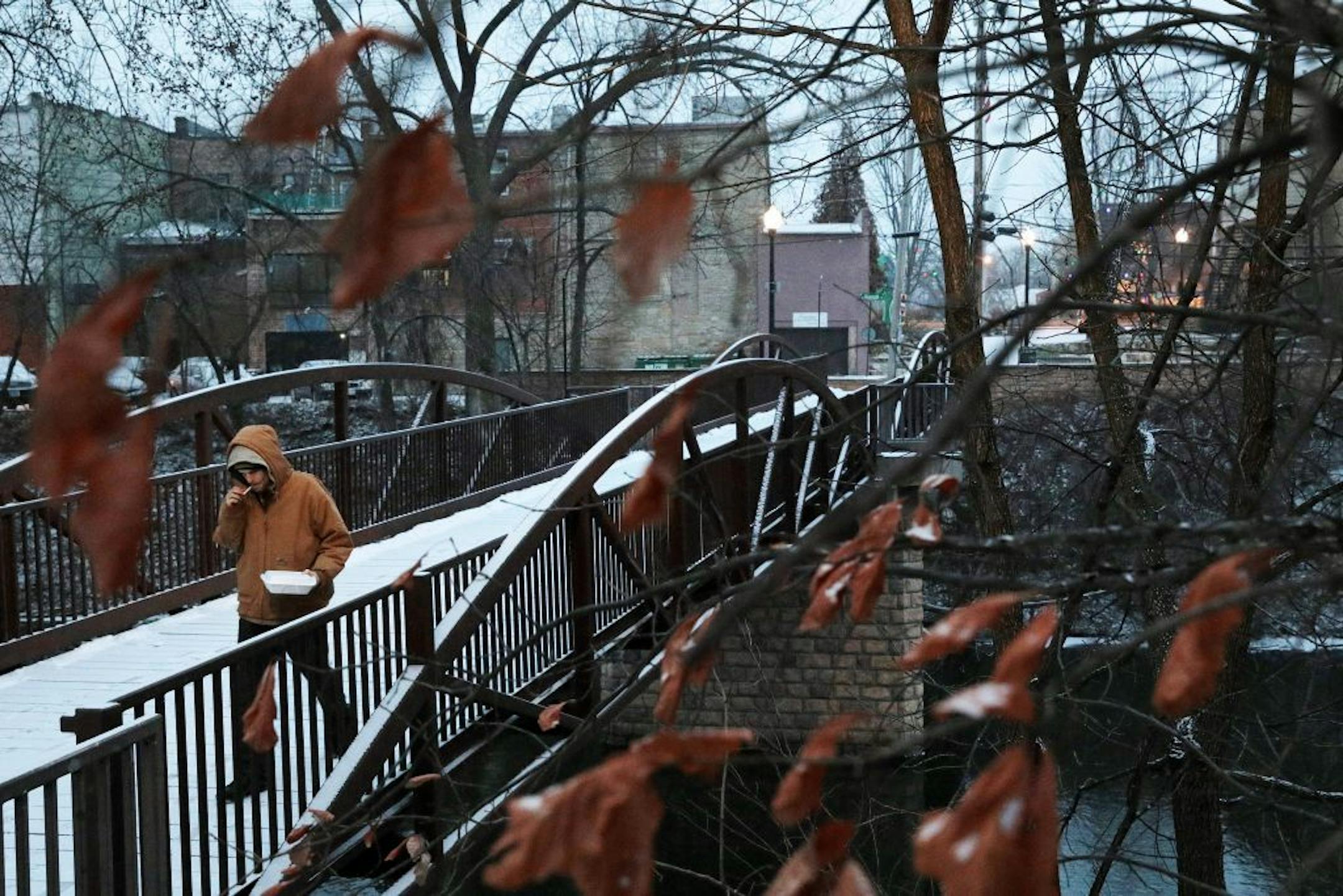 A man walks across the pedestrian bridge spanning over the Kinnickinnic River in Heritage Park.