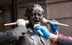 Workers from a company that maintains public art used brushes to add wax to the bronze statue of Vice President Hubert Humphrey in front of City Hall 