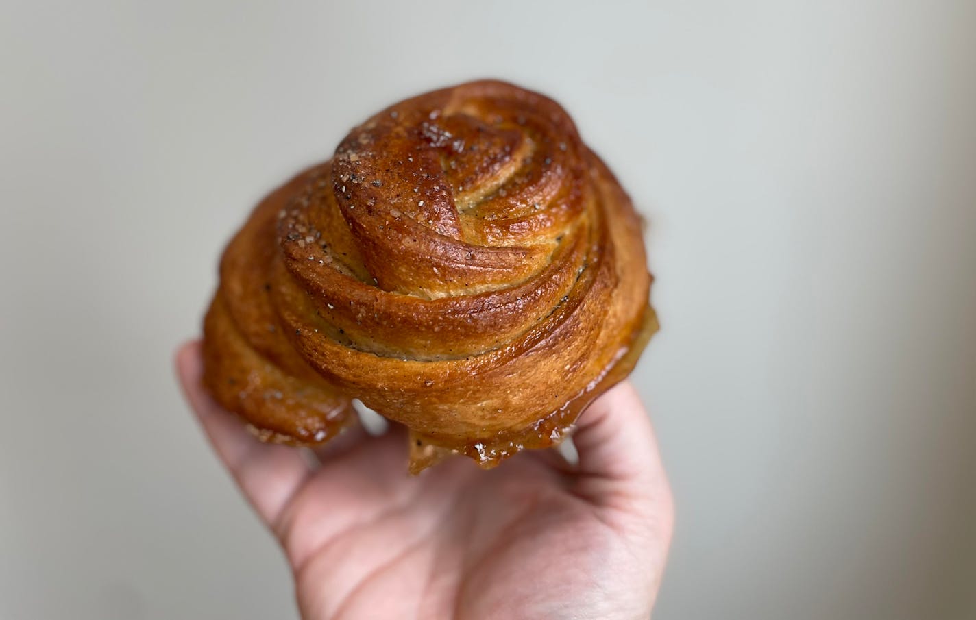 A hand holding a cardamom roll with edges dripping just a little bit of caramel.