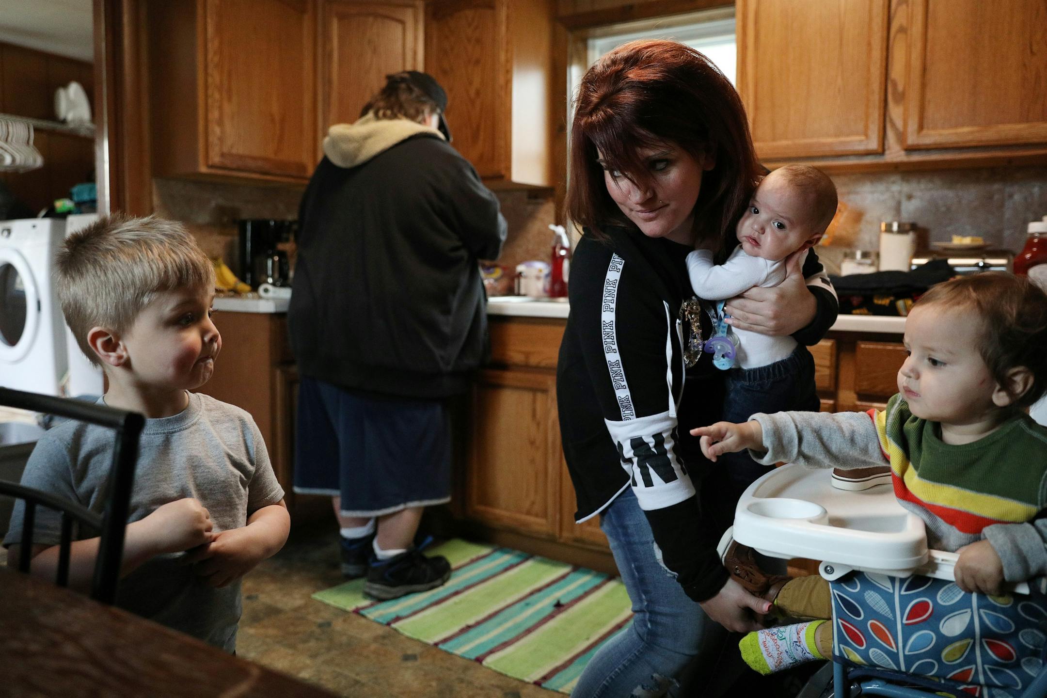 Ashley Benson, a mother of four who went through Sanford Bemidji Medical Center's First Steps program to help pregnant opioid addicts wean off their addictions, looked to her son Austin Boudreau, 3, left, while holding her son Graysen Burnette, 4-months, and trying to feed her other son Raymond Burnette, 15-months, as her uncle Bob Benson made dinner at their home.