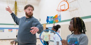 Anthony King, a tennis professional, teaches proper technique with an overhead swing to Zion Rootues during a InnerCity Tennis led physical education 