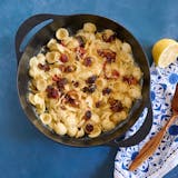 A pan with cheesy pasta and roasted cherry tomatoes next to a wooden spoon and bright napkin.