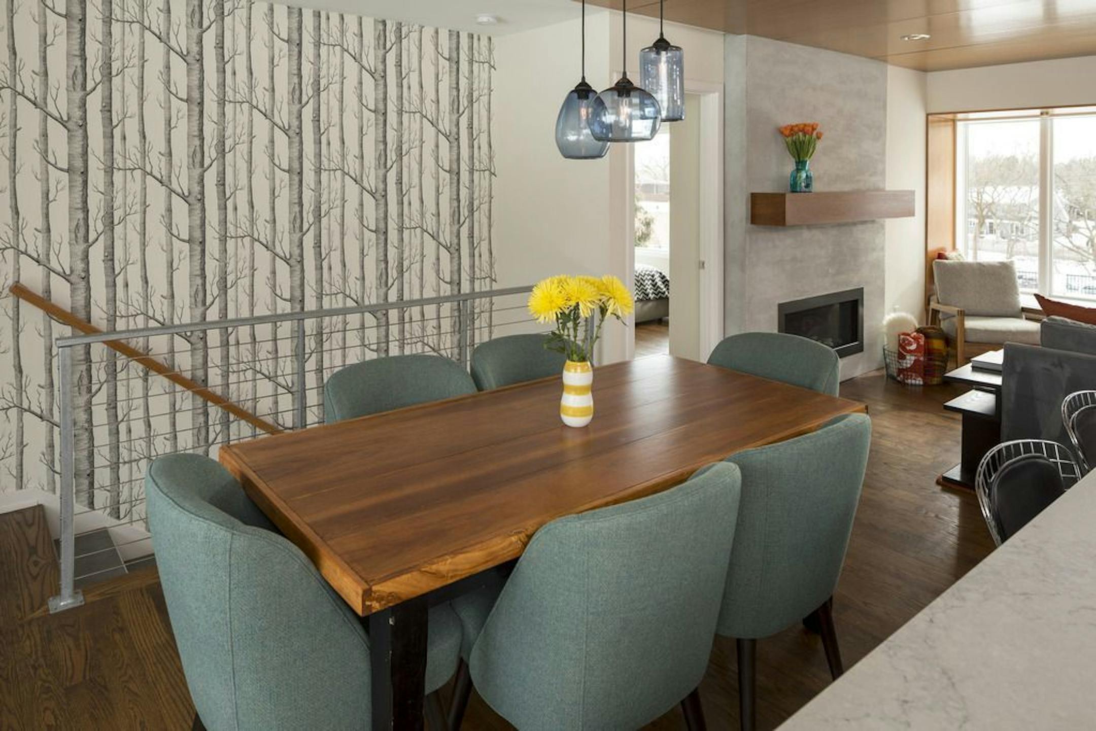 Dining area is accented with handblown blue glass pendants by Hennepin Made and Cole & Son "Woods" wallpaper covers the staircase wall.