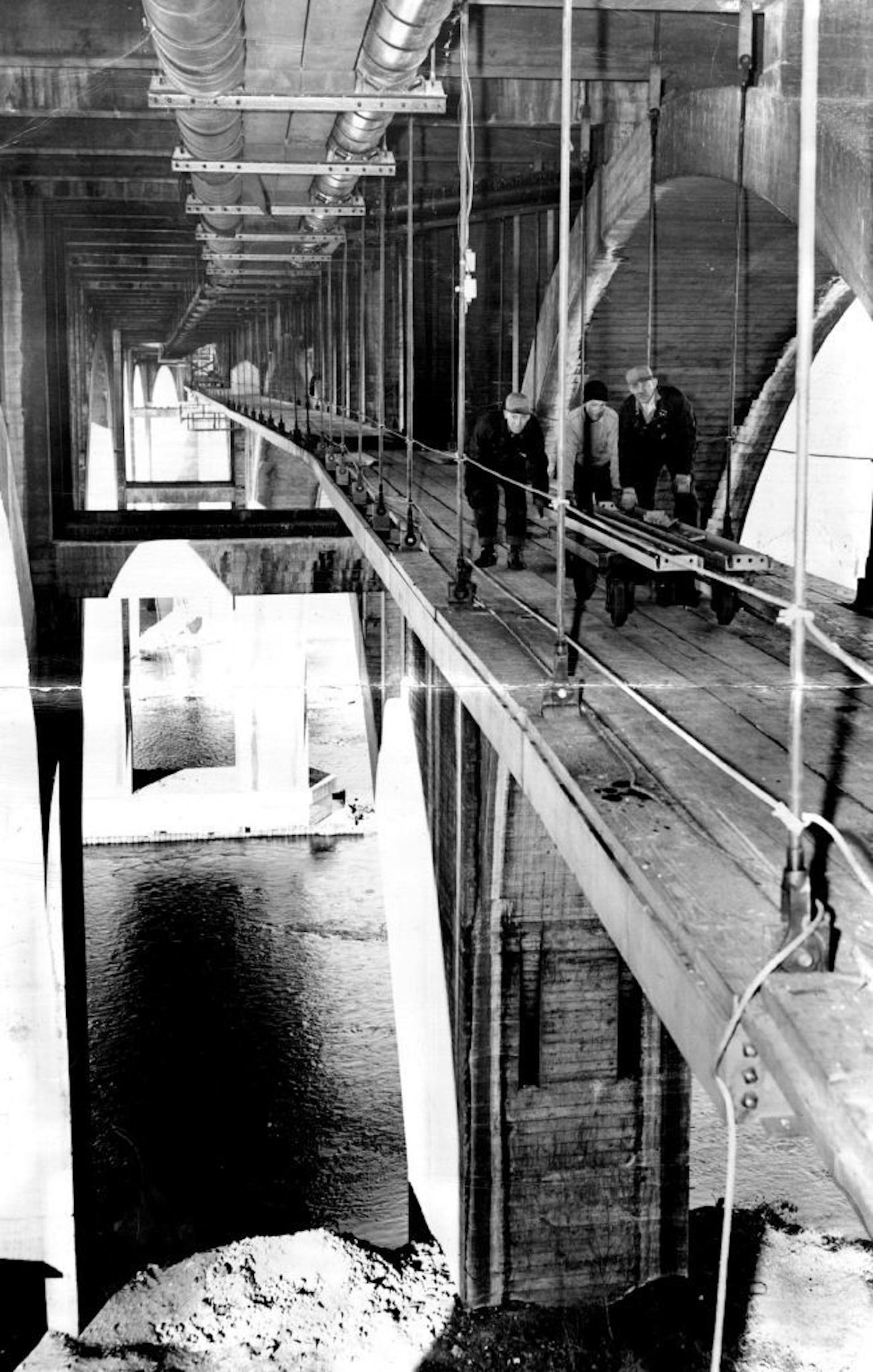 January 14, 1949 'BRIDGEâ€™ UNDER A BRIDGEâ€"A giant steel pipe support, looking like a catwalk and suspended by hangers, is being built under the Cedar avenue bridge as part of the job in putting a 54-inch water main across the river. The men are building, it from the west approach and now are workmen should slip. January 15, 1949 Minneapolis Star Tribune