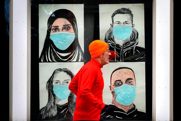 A runner passes by a window displaying portraits of people wearing face coverings to help prevent the spread of the coronavirus in Lewiston, Maine.