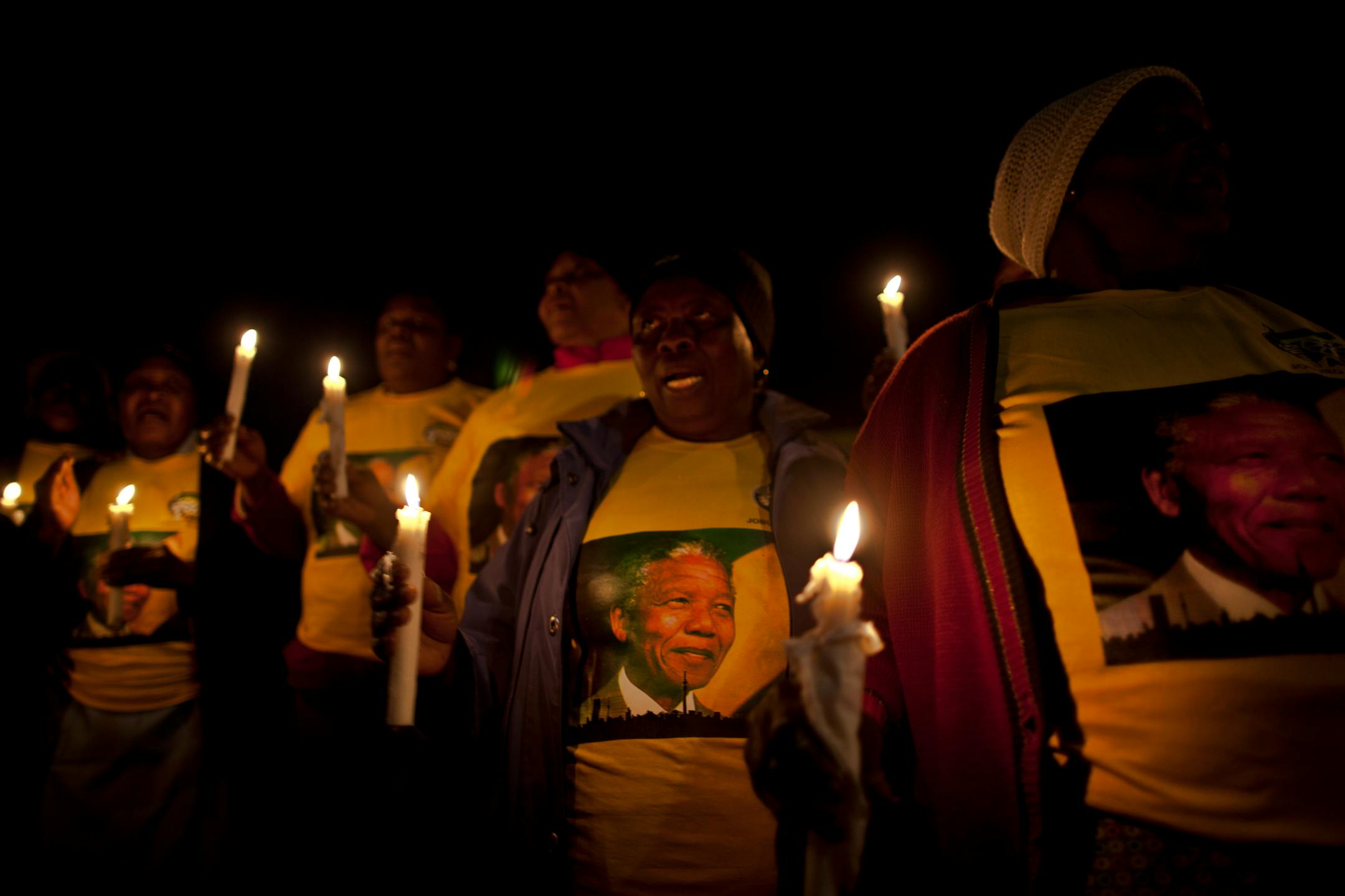 ANC women's organization members, hold candles and chant prayers to honor former South African President Nelson Mandela in front of his house in the Soweto township, on the outskirts of Johannesburg, South Africa, Thursday, July 4, 2013. Mandela remains in a critical condition in a hospital in Pretoria. (AP Photo/Muhammed Muheisen)