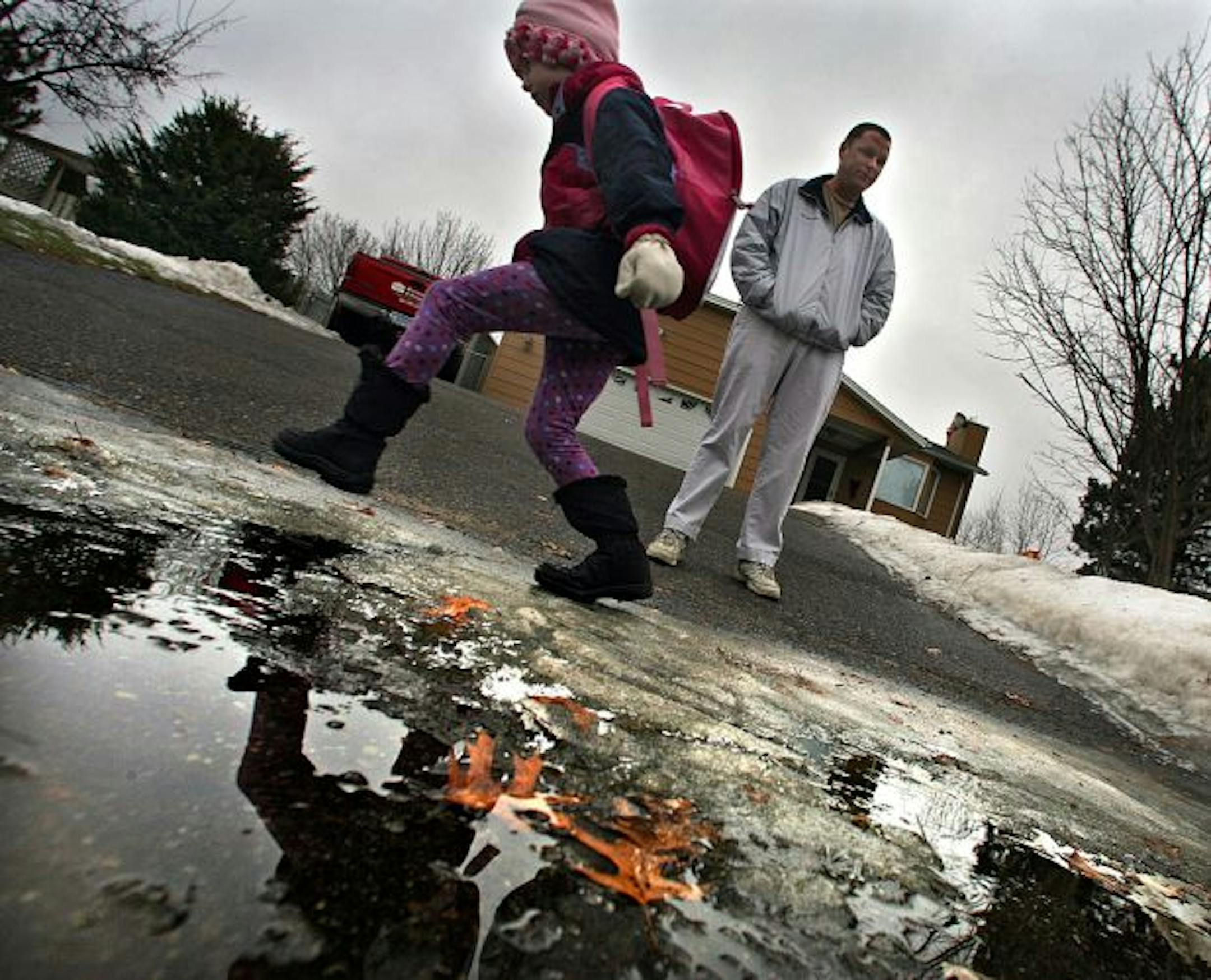 Lila Bystrom, 5, played in puddles as she waited for the school bus. Her father, Tom Bystrom, has become a stay-at-home dad since seeing his work slow down. He and his wife pulled their two daughters out of day care, saving about $800 a month.
