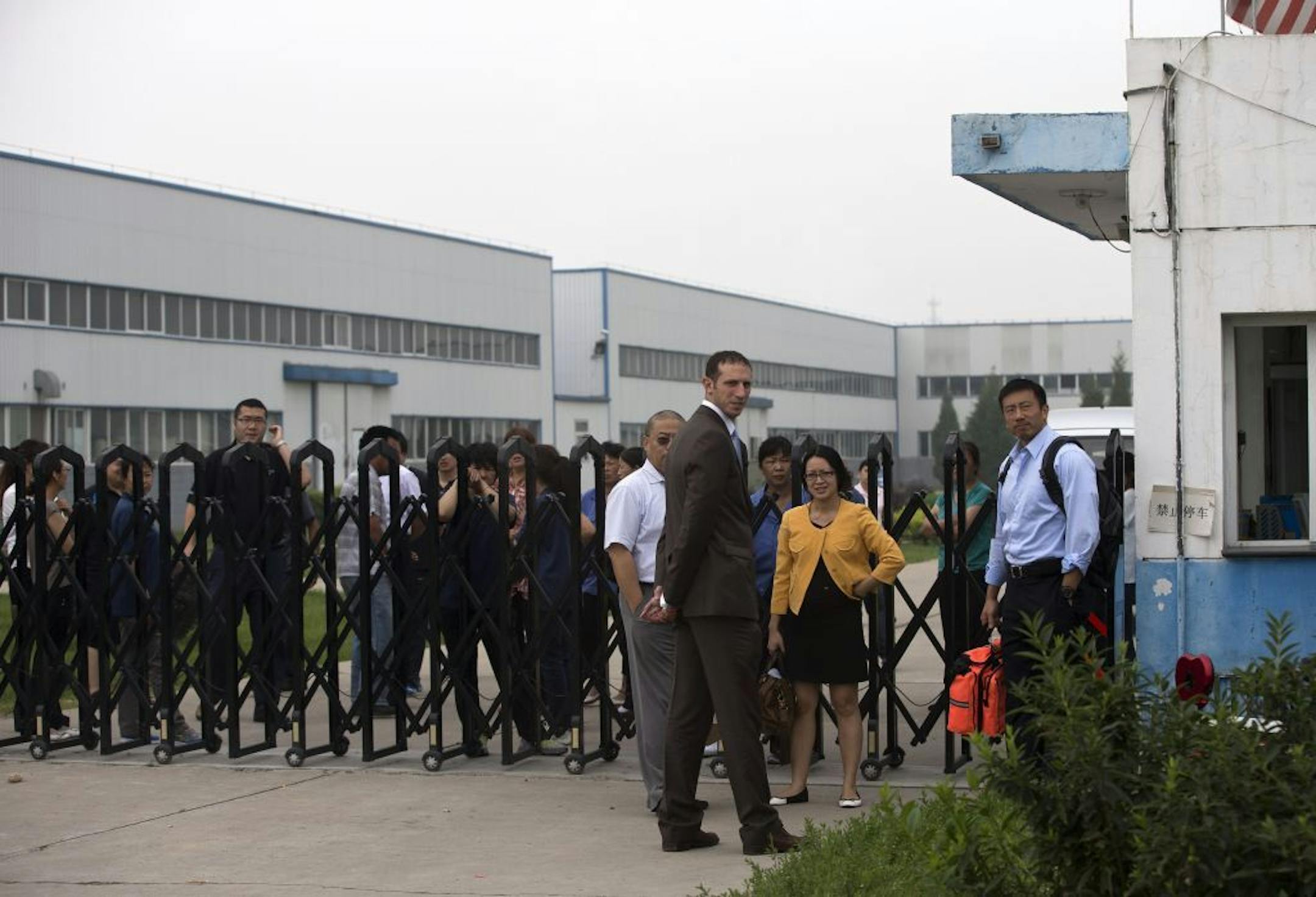 U.S. Embassy employees stand outside the closed gate at Specialty Medical Supplies plant where American Chip Starnes, co-owner of the plant, not in picture, is being held hostage at the Jinyurui Science and Technology Park on the outskirts of Beijing, China Monday, June 24, 2013.
