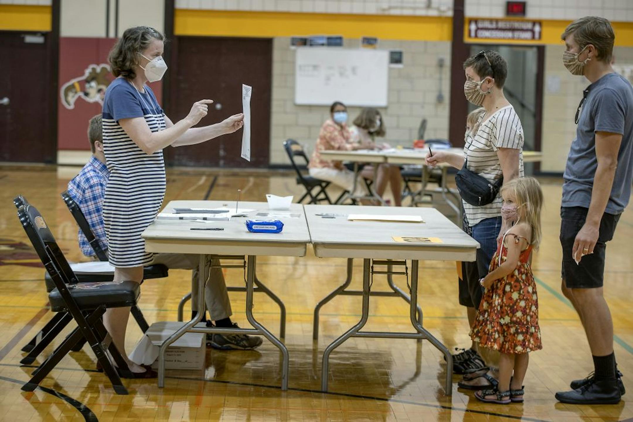 Election volunteer Brenda Scott went through the voting process with Nora Jenneman and Ryan Seibold as their children Fern Seibold, 5 and Rainer Seibold, 10 looked on at the Roosevelt High School polling location, Tuesday, August 11, 2020 in Minneapolis, MN.