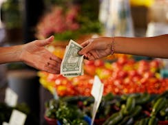 Person hands over money to buy produce at farmers market.