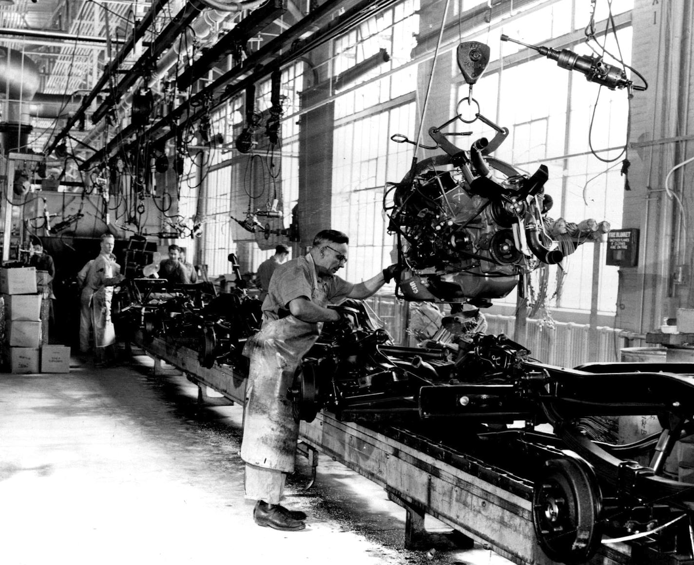 April 3, 1955 Power Equipment does heavy work at Ford Plant, Worker guides engine onto chassis in "motor drop" operation. March 28, 1955