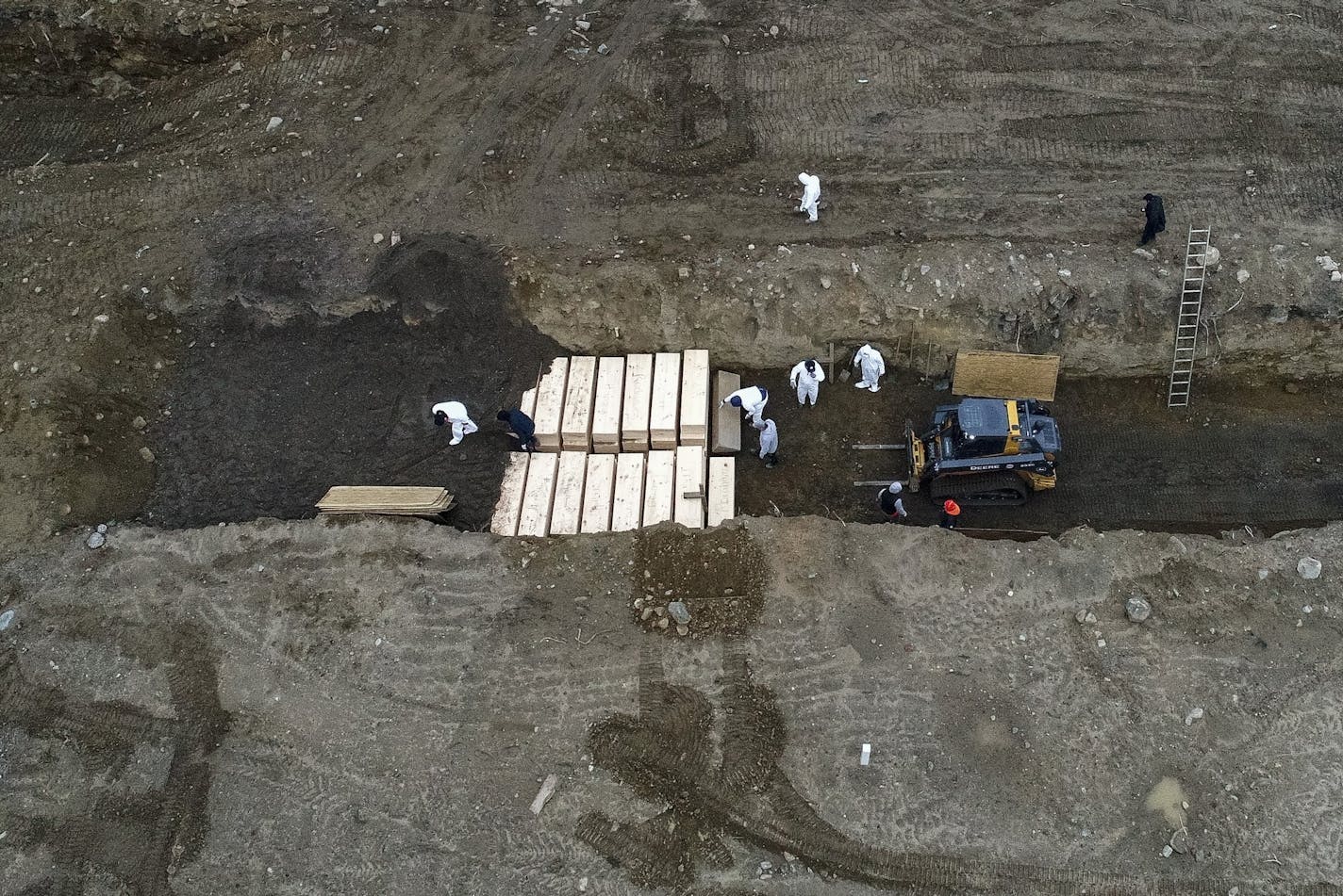 FILE - In this April 9, 2020, file photo, workers wearing personal protective equipment bury bodies in a trench on Hart Island in the Bronx borough of New York. The official death toll from the coronavirus soared in New York City on Tuesday, April 14, 2020, after officials began including people who probably had COVID-19, but died without ever being tested. (AP Photo/John Minchillo, File)