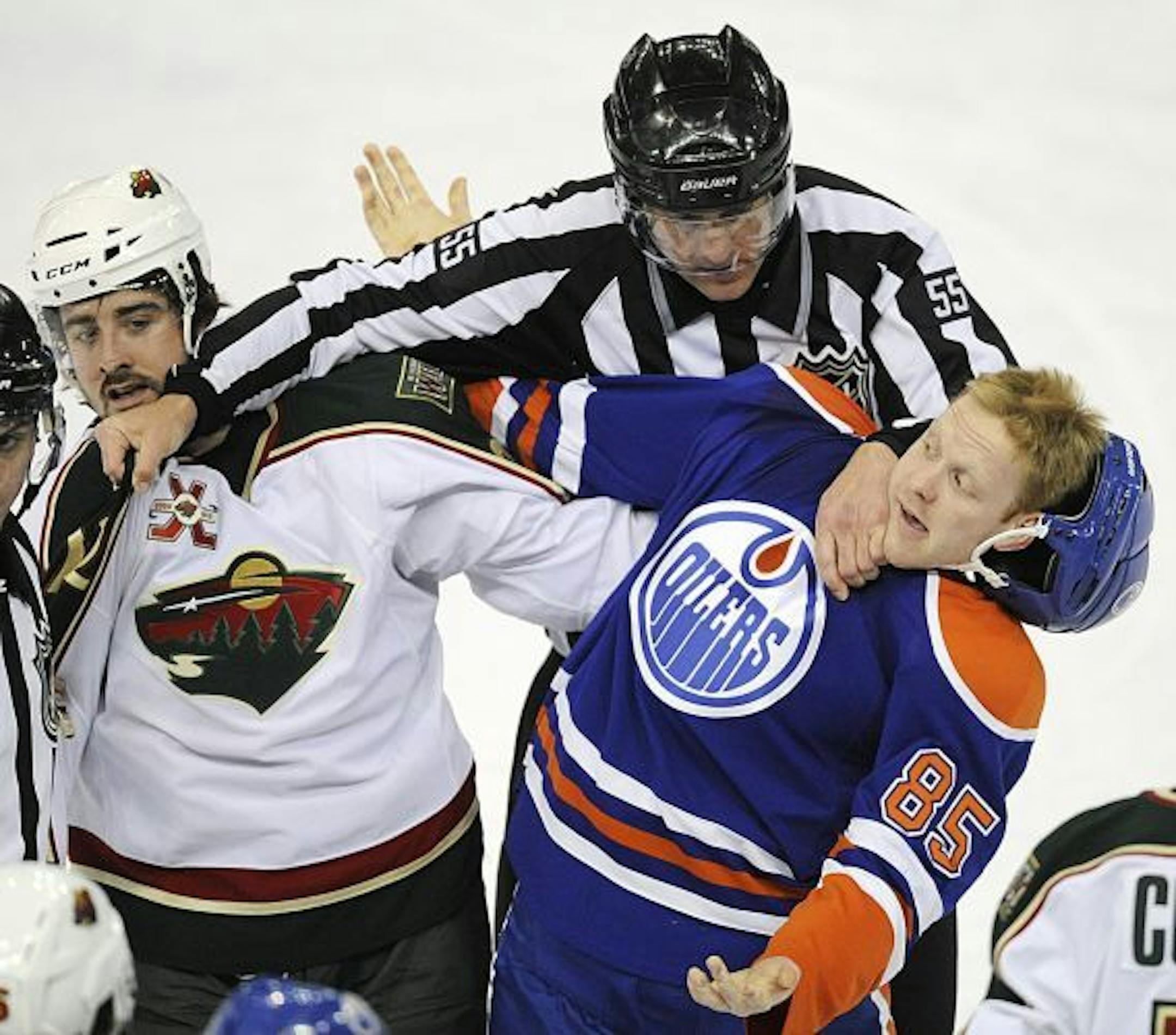 Linesman Shane Heyer, center, separates Minnesota Wild's Cal Clutterbuck, left, and Edmonton Oilers' Liam Reddox during first-period NHL hockey game action in Edmonton, Alberta, on Friday, April 8, 2011.