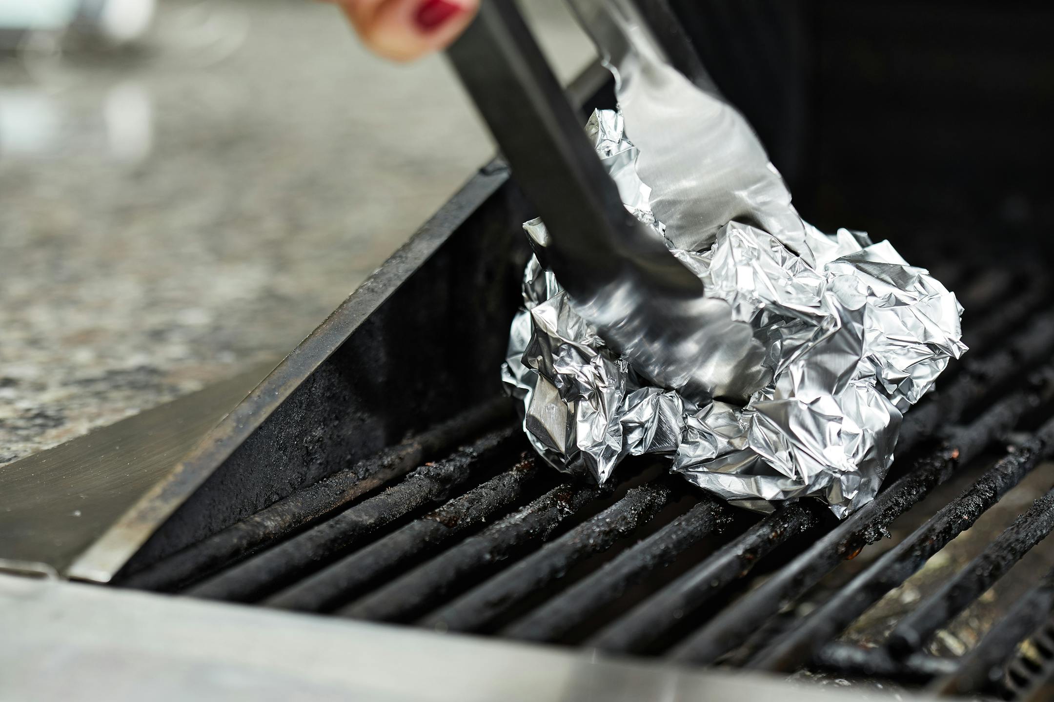 Demonstrating how to clean the grill with a ball of crumpled foil (about the size of a navel orange) held in a pair of long-handled tongs.