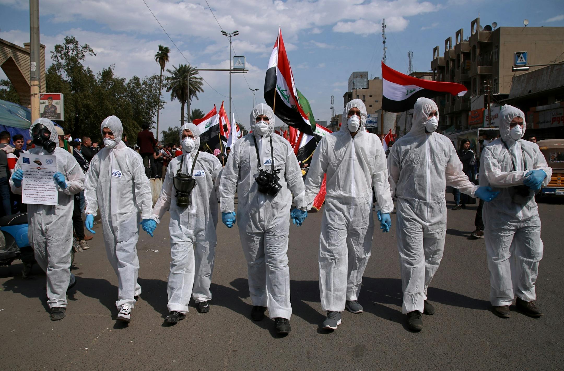 FILE - In this March 1, 2020 file photo, anti-government protesters wear hazmat-like suits and gas masks during a rally in Baghdad, Iraq. As 2019 gave way to 2020 in a cloud of tear gas, and in some cases a hail of bullets, from Hong Kong to Baghdad, from Beirut to Barcelona and Santiago, it seemed civil disobedience and government crackdowns on protests would dominate the international landscape. Then came the coronavirus. But some protesters are trying to keep their movements alive, adjusting
