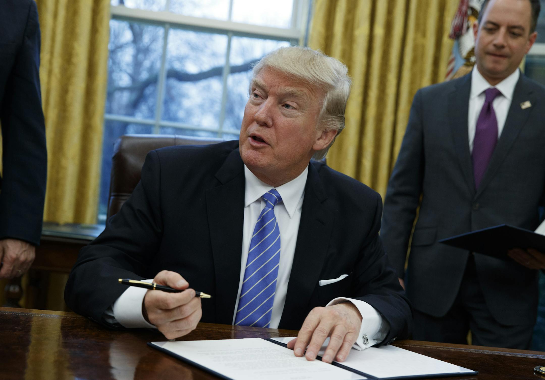 President Donald Trump signs an executive order to withdraw the U.S. from the 12-nation Trans-Pacific Partnership trade pact agreed to under the Obama administration, Monday, Jan. 23, 2017, in the Oval Office of the White House in Washington. (AP Photo/Evan Vucci)