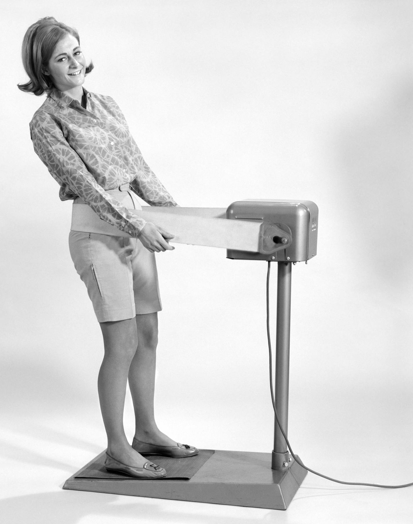 AAM1AK 1960s SMILING YOUNG WOMAN STANDING ON WEIGHT REDUCING VIBRATING EXERCISE MACHINE LOOKING AT CAMERA ClassicStock / Alamy Stock Photo ORG XMIT: AAM1AK