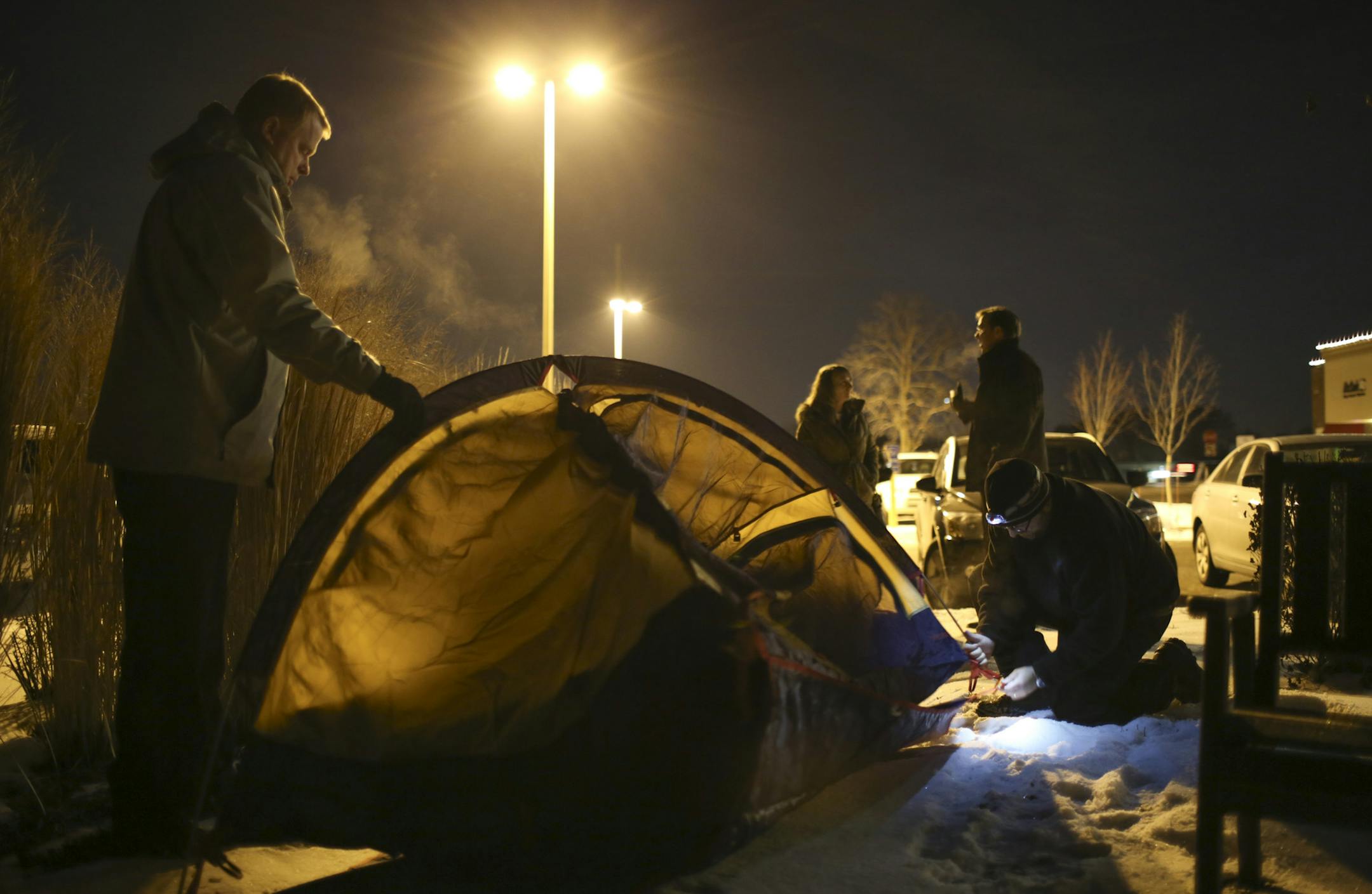 Erik Hagestuen, left, offered a steadying hand while Mark Schmid, Pastor at St. Philip the Deacon Lutheran Church, kneeled to set up his tent before sleeping outside the IOCP building Wednesday night. ] JEFF WHEELER ‚Ä¢ jeff.wheeler@startribune.com With temperatures dipping well into the teens overnight, about two dozen hearty souls slept out in tents, cardboard boxes, or their cars in the parking lot of Interfaith Outreach & Community Partners and their ReSale 101 store in Plym