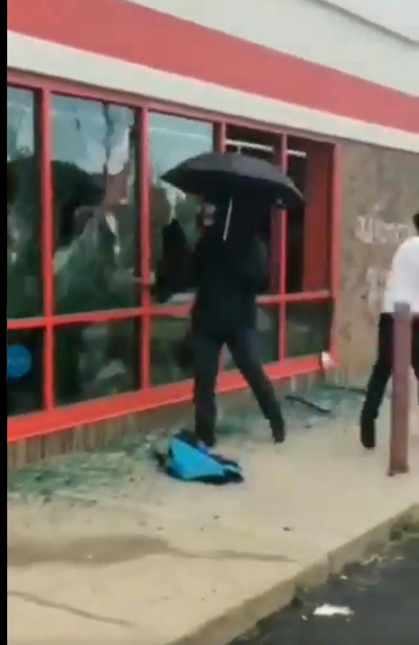 A still from a video shows a man with an umbrella and gas mask breaking windows at the AutoZone on Lake Street during protests in the wake of George Floyd's death. (Twitter/Javier Morillo)