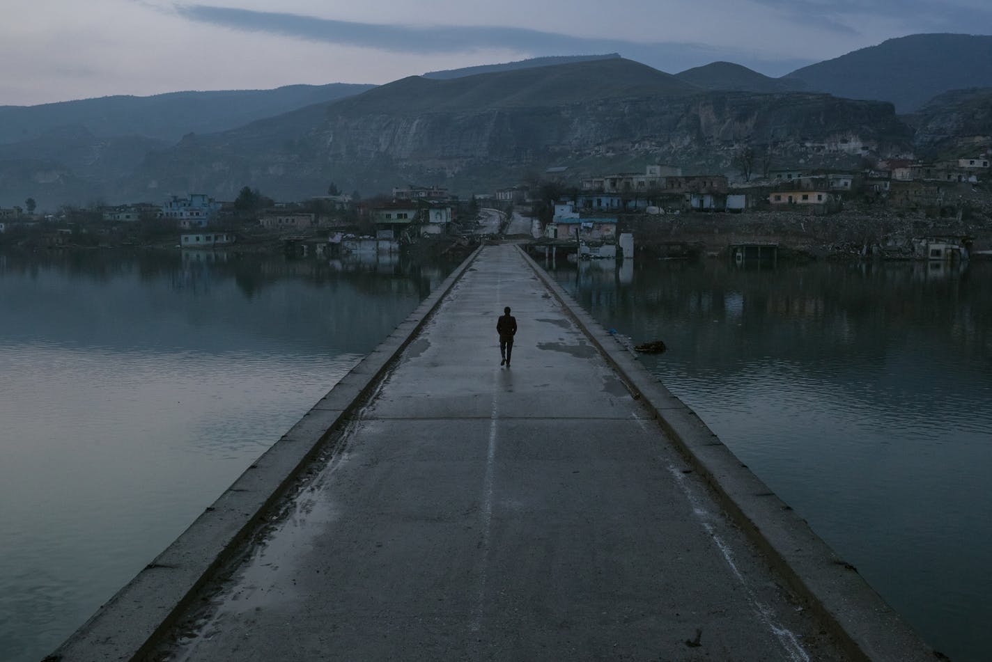 A resident walks across a bridge to the old town of Hasankeyf, Turkey, partially submerged by the Tigris River, Feb. 20, 2020. In his push for economic development, Turkey's president has flooded the archaeological gem of Hasankeyf and displaced thousands of families. (Mauricio Lima/The New York Times)