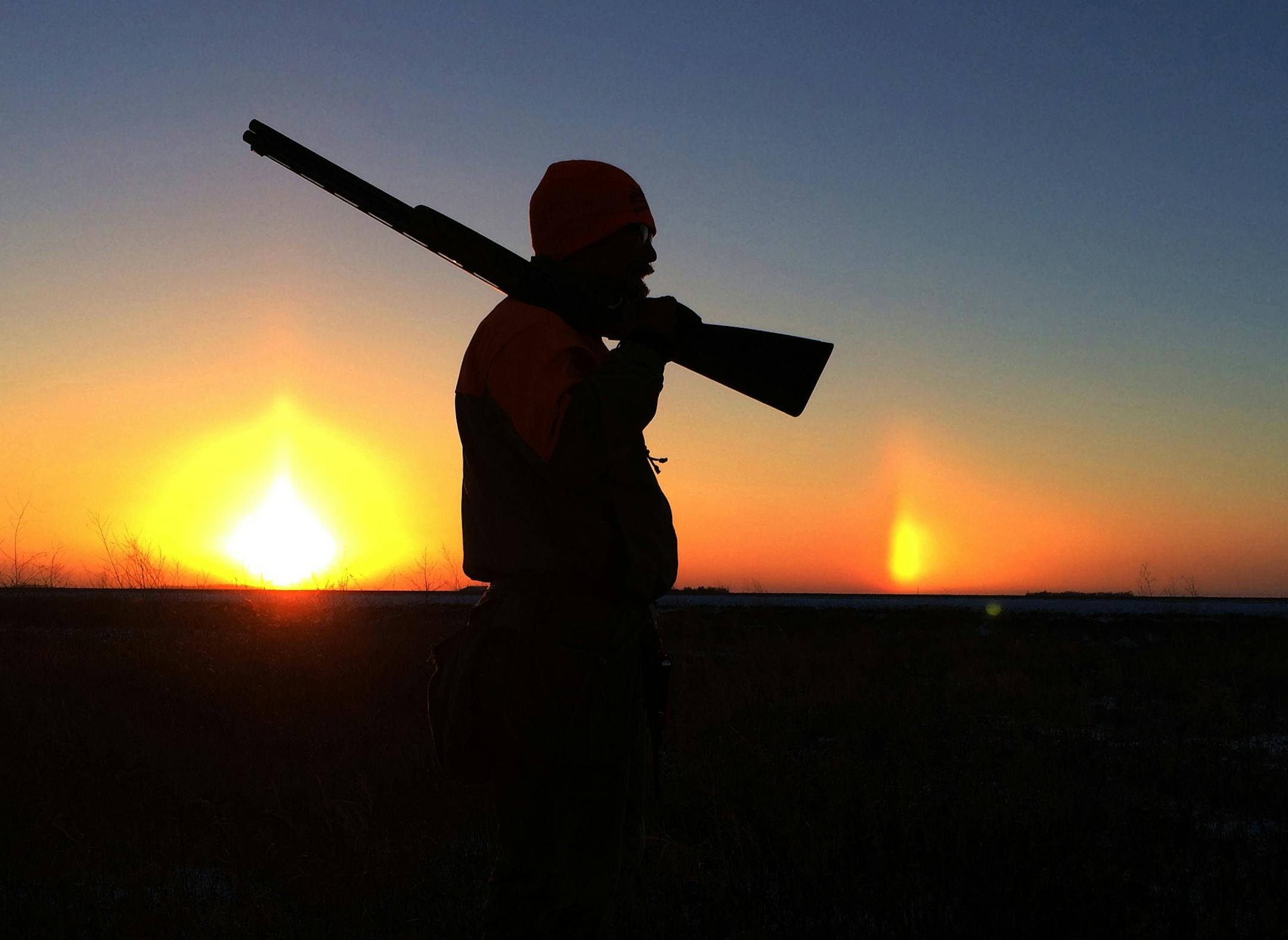Bob St. Pierre of Hugo is bracketed by the setting sun and a sundog on a cold day in northwestern Minnesota.