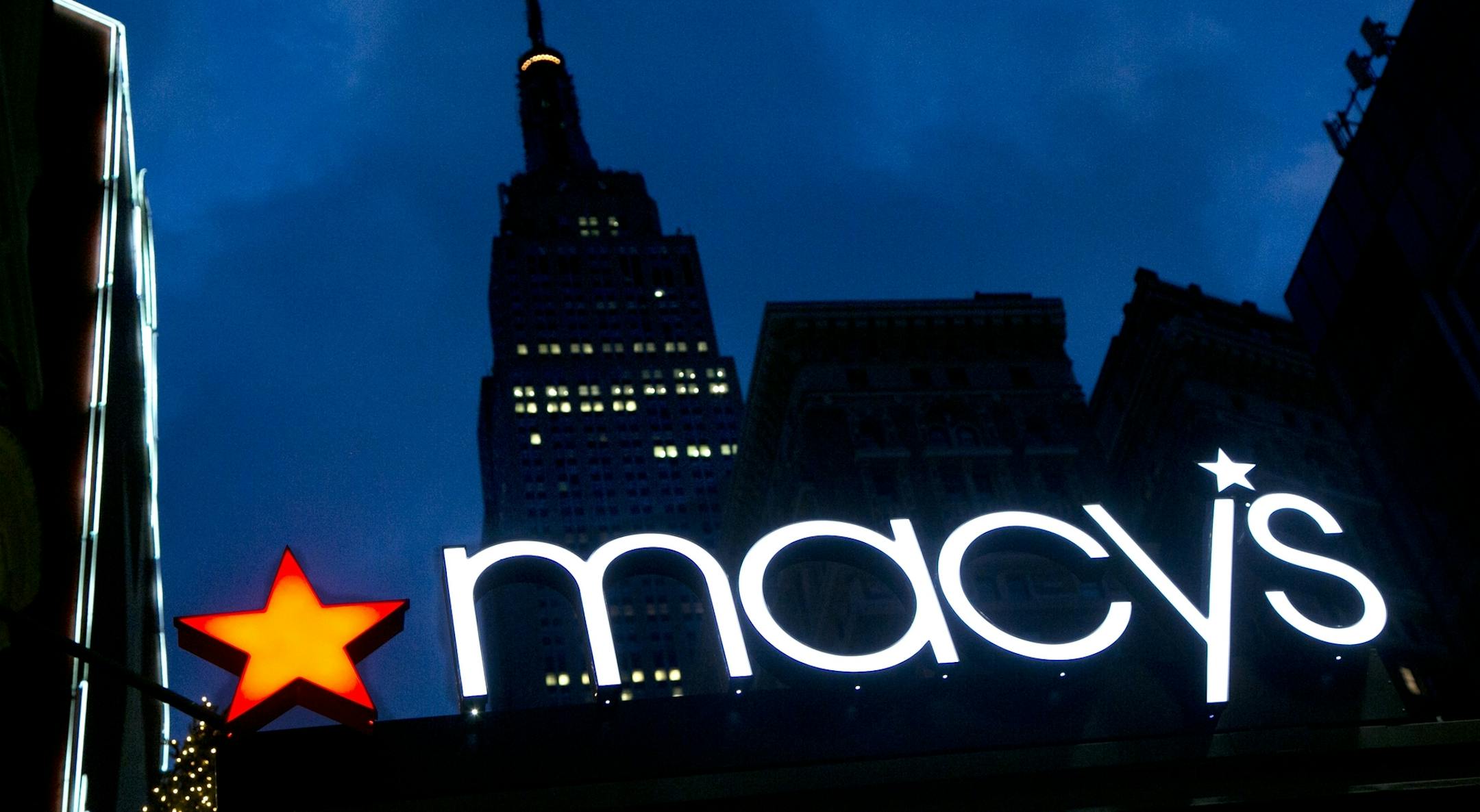 FILE - In this Nov. 21, 2013, file photo, with the Empire State building in the background, the Macy's logo is illuminated on the front of the department store in New York.
