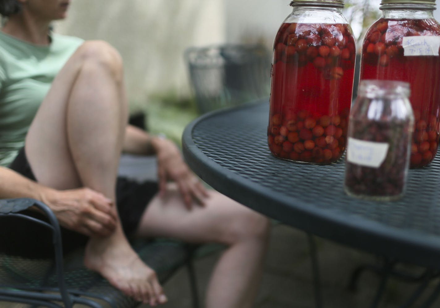 Kirsch, a liquid made with fermented cherries, sits on the table next to Mary Ann Crolley, who along with her husband Charlie Underwoood, a retired teacher who taught for 41 years, are veteran foragers and seen outside their home Thursday, July 24, 2014, in Minneapolis, MN.] (DAVID JOLES/STARTRIBUNE) djoles@startribune Foraging - the act of picking berries, flowers and anything else that looks edible off the road for consumption - is on the rise in Minneapolis. The community that does it is smal