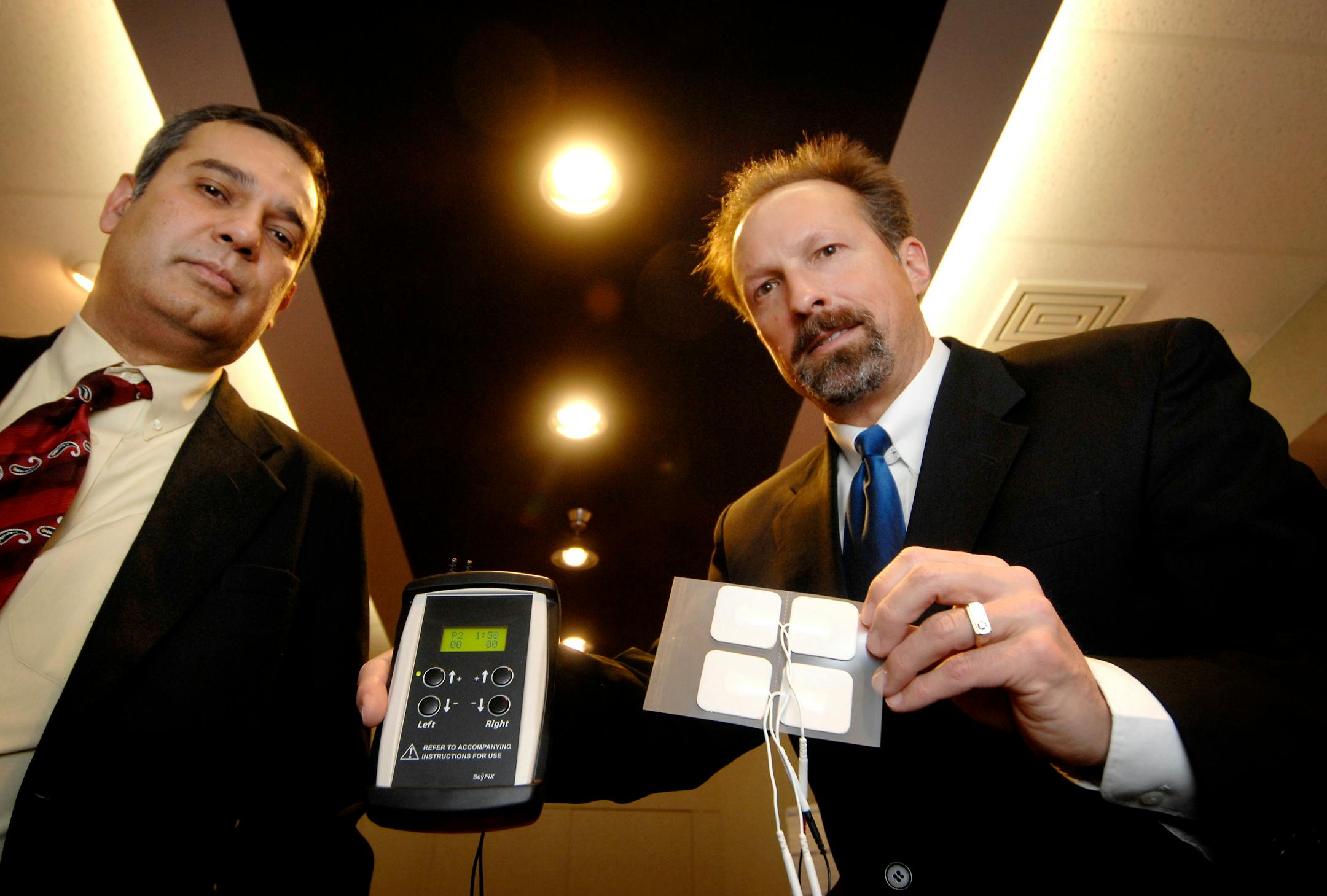ScyFix President Dr. Darrell DeMello, left, and founder Thomas Harold with the microcurrent stimulation therapy device they developed. It is now in clinical trials for treating macular degeneration and retinitis pigmentosa.