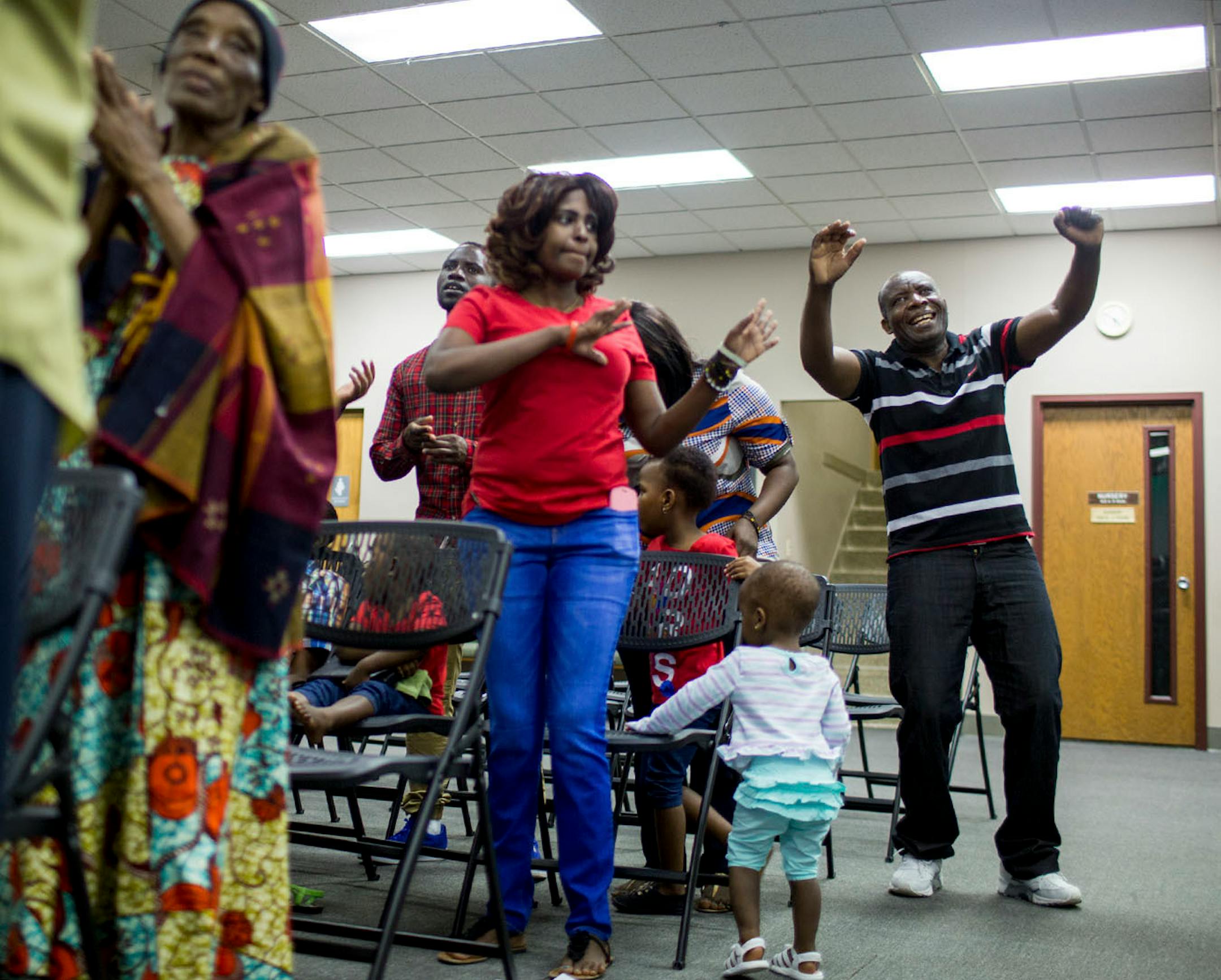 Ladislas Mihigo (right) raises his hands while listening to his daughters sing about God, during the church service for African refugees, at Bethel Christian Fellowship Church.