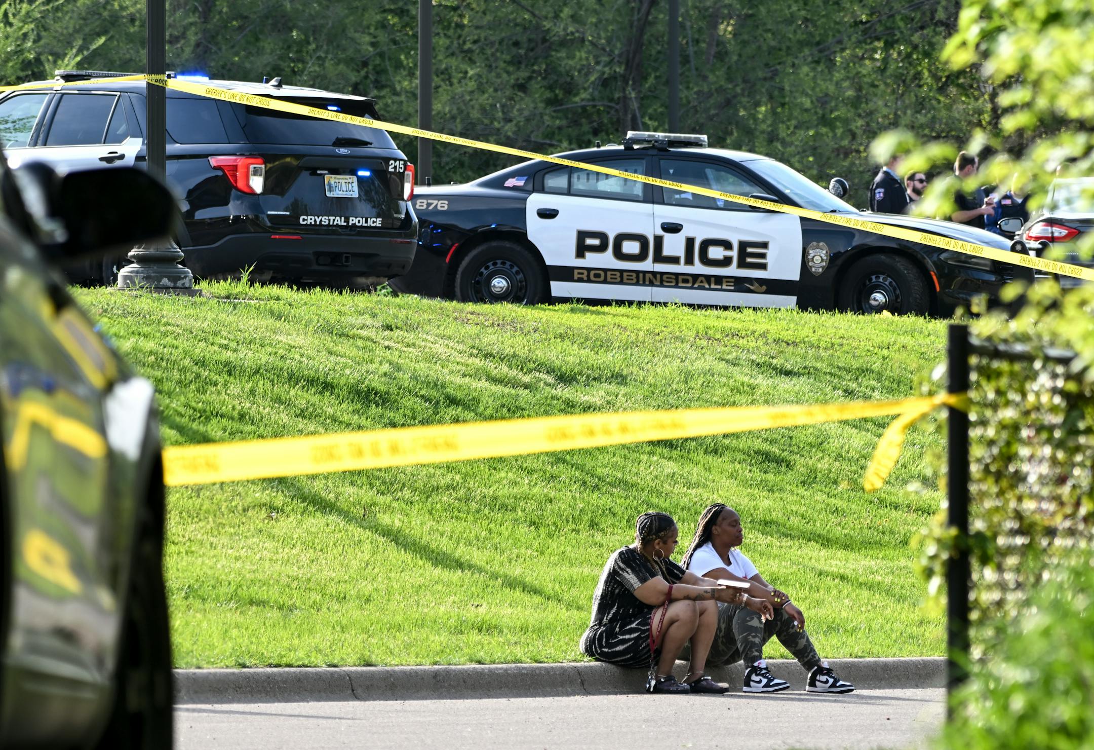 People sat on a curb at Lakeview Terrace Park near the scene of a fatal shooting Thursday on County Road 81 in Robbinsdale.