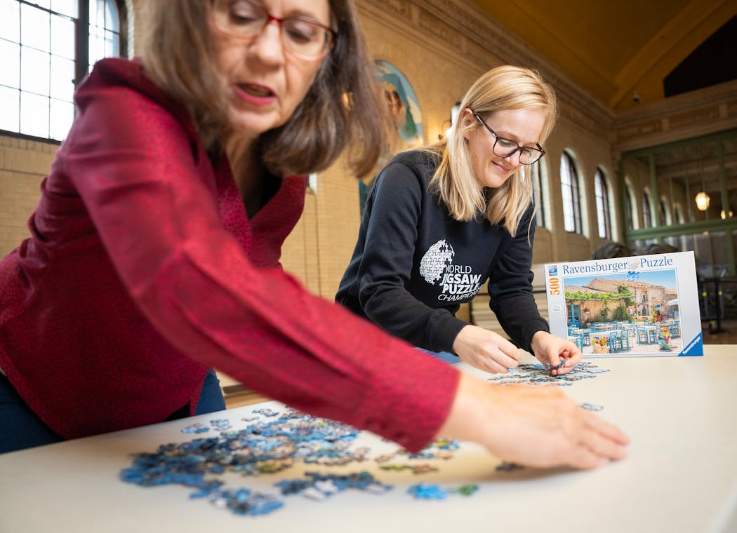 Cynthia Schreiner Smith, chair of the St. Paul Winter Carnival jigsaw competition, left, and Sarah Schuler, a top-ranked puzzler, flipped puzzle pieces inside St. Paul’s Union Depot, where this winter’s Winter Carnival puzzle contest will be held.