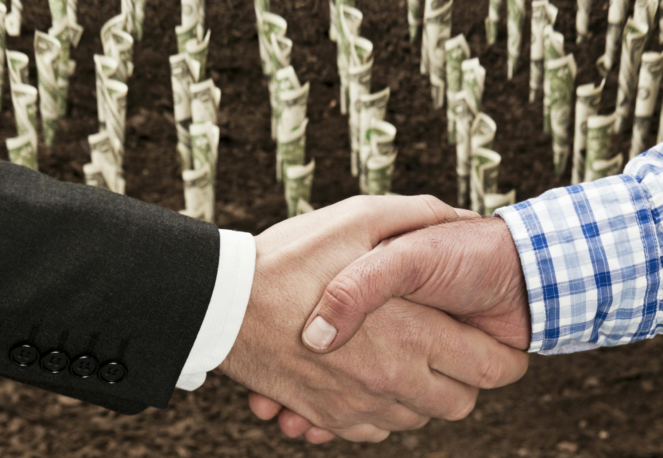 Farmer and businessman shaking hands in front of field of money