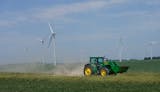 A farmer drives his tractor along a gravel road, below wind turbines from the Fenton Wind Farm, where power line congestion is increasingly shutting down and leading to significant tax revenue decline Wednesday, June 29, 2022 in Murray County, Minn.