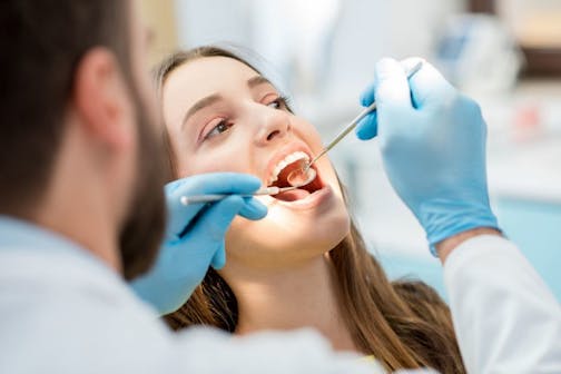 Dentist examining patient teeth with a mouth mirror and dental excavator. Close-up view on the woman's face