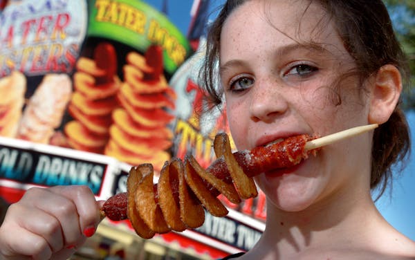Jenna Zellmer takes a bite out of a Tater Dog ($7.75), a hot dog wrapped in a potato spiral, at Texas Tater Twisters.