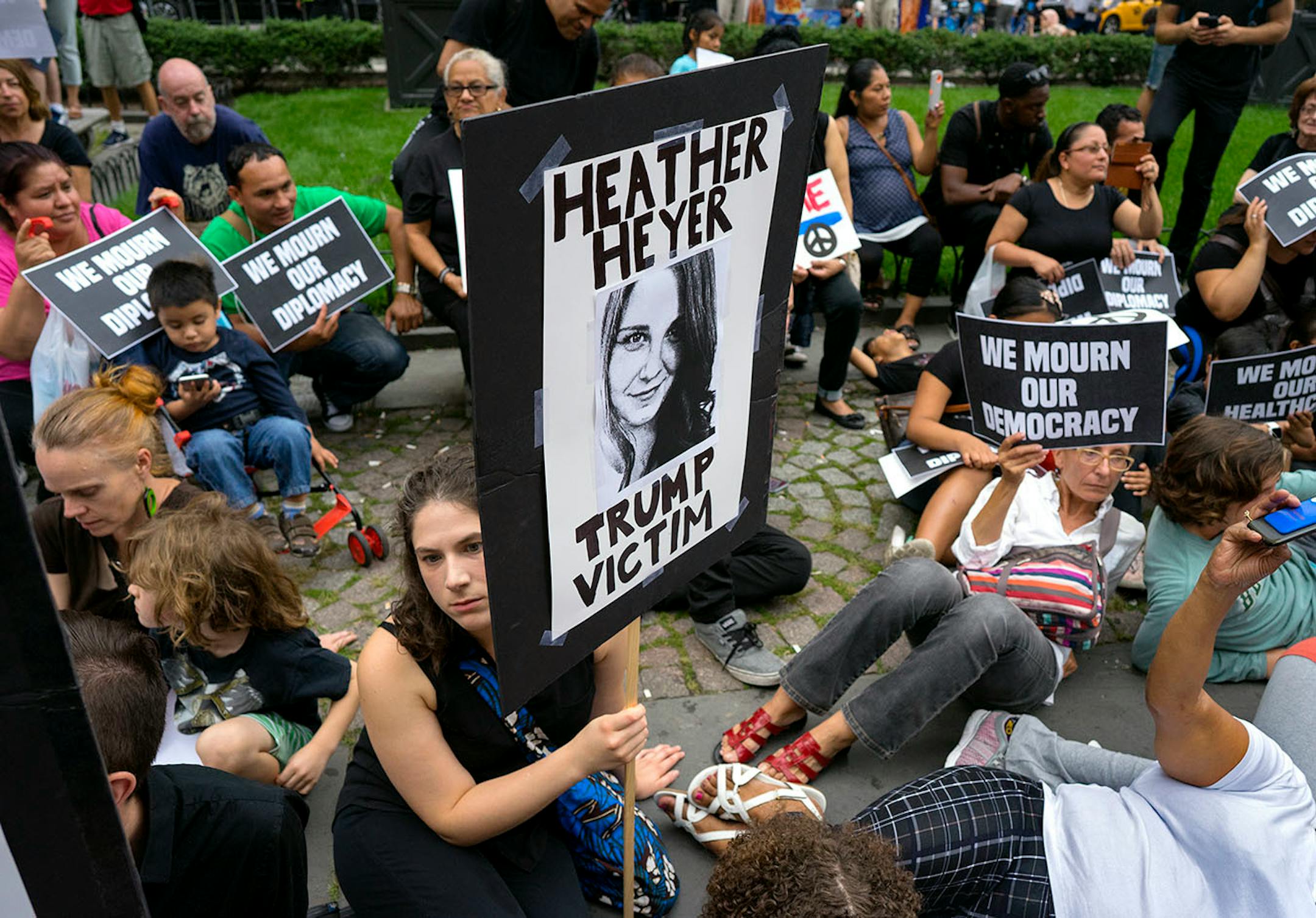 Protestors gathering at 59th Street and 5th Avenue in New York sit during a moment of silence Monday, Aug. 14, 2017, as they protest President Donald Trump not far from Trump Tower. One person holds a sign referring to Heather Heyer who was killed in Charlottesville, Va., on Saturday, after a car plowed into a crowd.