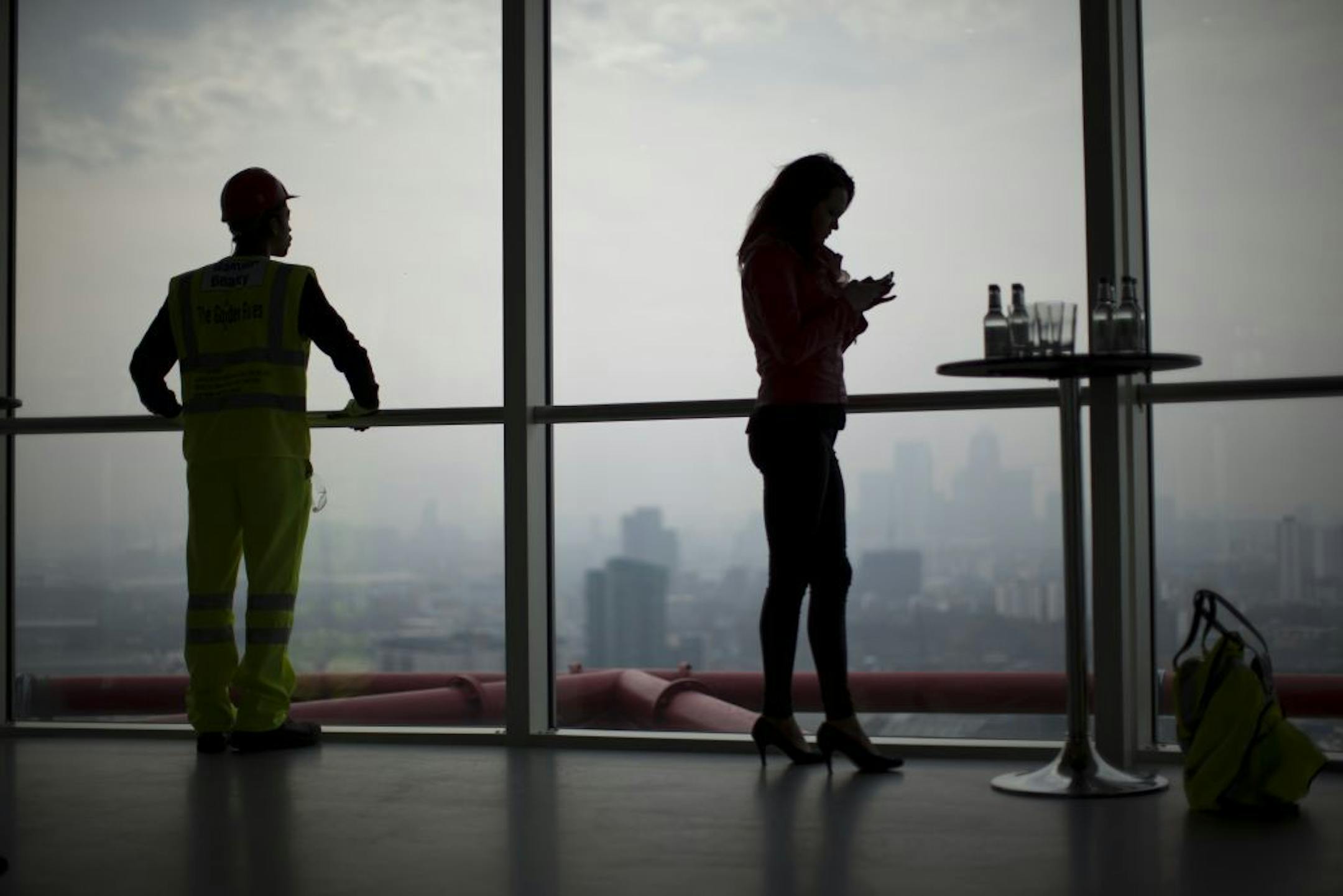 Smog blanketing London's Canary Wharf business district forms a backdrop for two workers at the Queen Elizabeth Olympic Park on Wednesday, April 2, 2014.