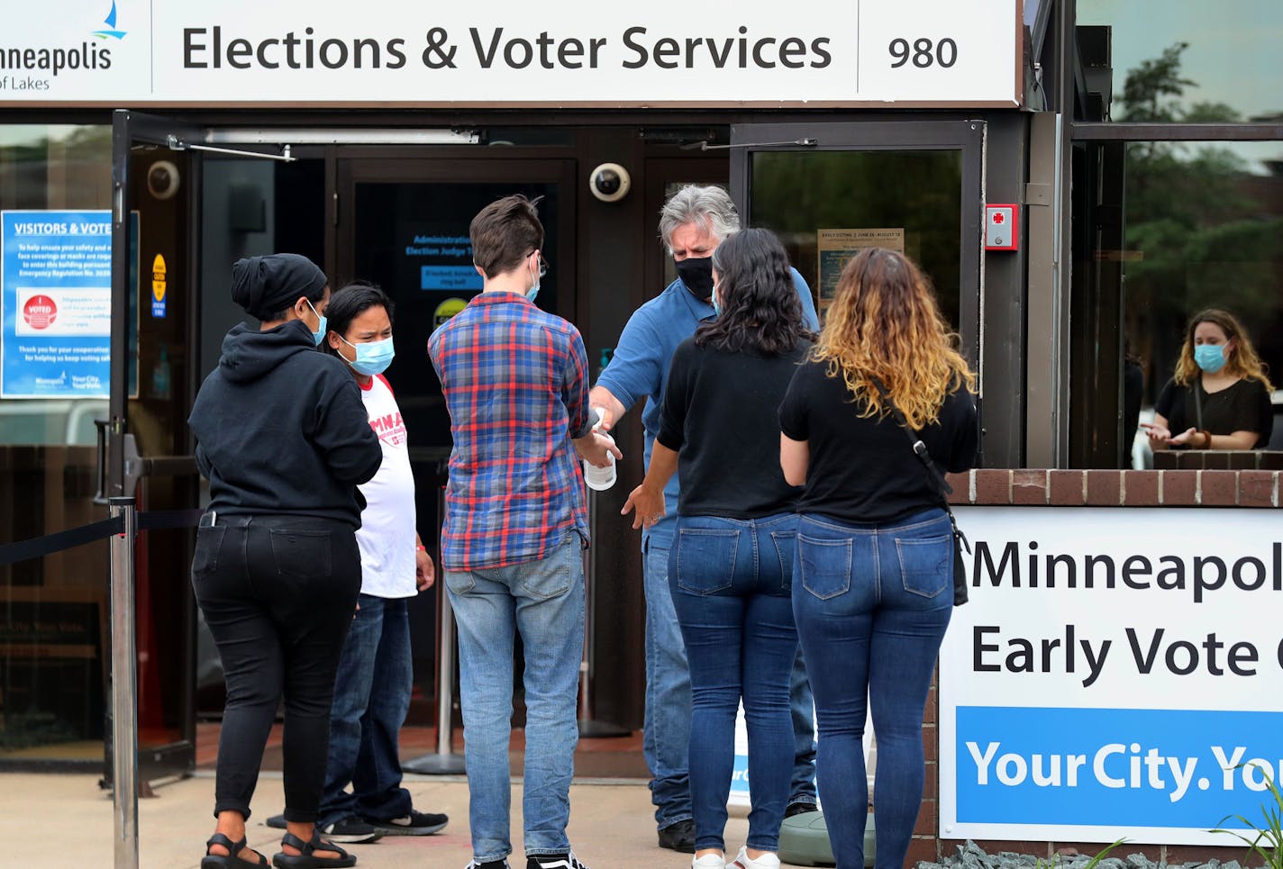 Election official John Jovanovich sprays hand sanitizer on walk-up early voters for the State Primary at Minneapolis Elections & Voter Services Friday in Minneapolis.