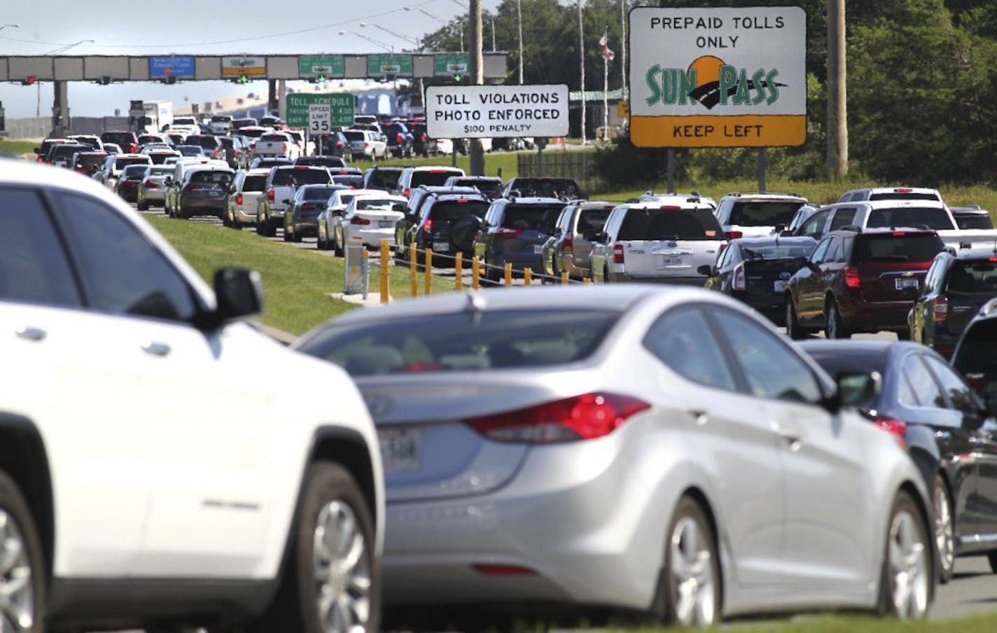 In a Saturday, June 10, 2017 photo, southbound motor vehicles heading for Destin and south Walton County, Florida are backed up at the Mid-Bay Bridge toll plaza in Niceville, Fla. The approximately 3.5-mile-long bridge spans Choctawhatchee Bay and is particularly crowded on Saturdays during the summer as vacationers coming south from State Road 85 and Interstate 10 try to cross the bay to check in to condominiums along the coast.