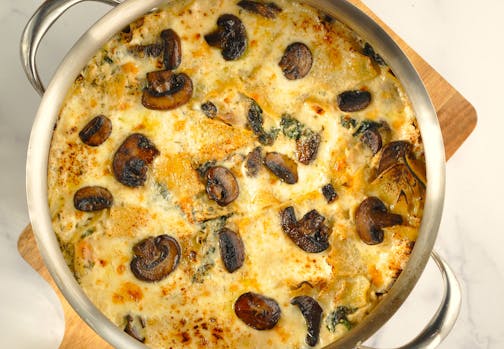 A round stainless-steel pan, sitting on a cutting board, holds a cheesy, creamy chicken, spinach and mushroom lasagna, which can be made in one pot on the stove.