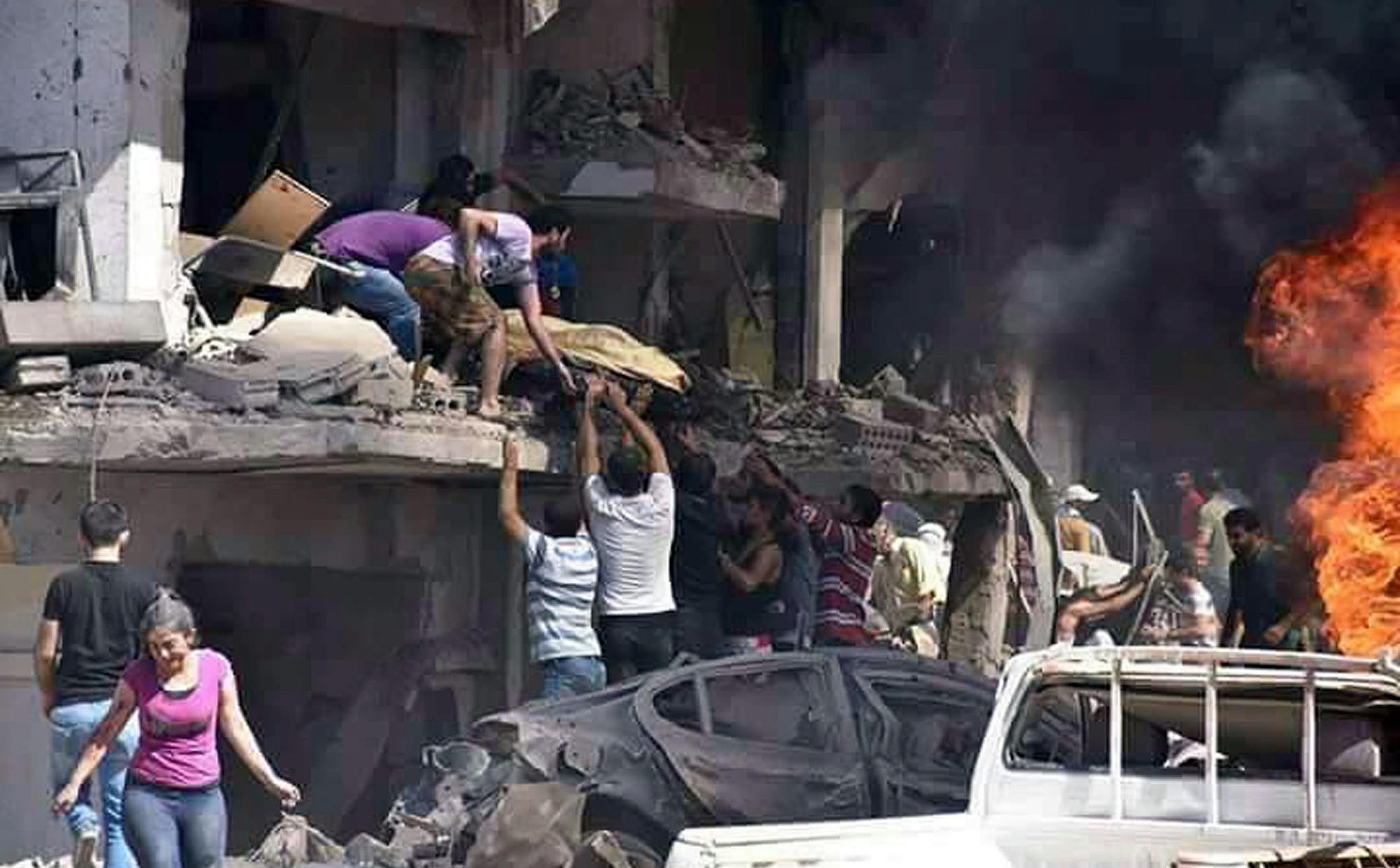 In this photo released by the Syrian official news agency SANA, Syrians carry the body of a victim from a building damaged in twin bombings struck Kurdish town of Qamishli, Syria, Wednesday, July 27, 2016. Bombings struck a crowd in a predominantly Kurdish town in northern Syria on Wednesday, killing 44 people and wounding dozens more, Syria's state-run news agency and Kurdish media reported. (SANA via AP)