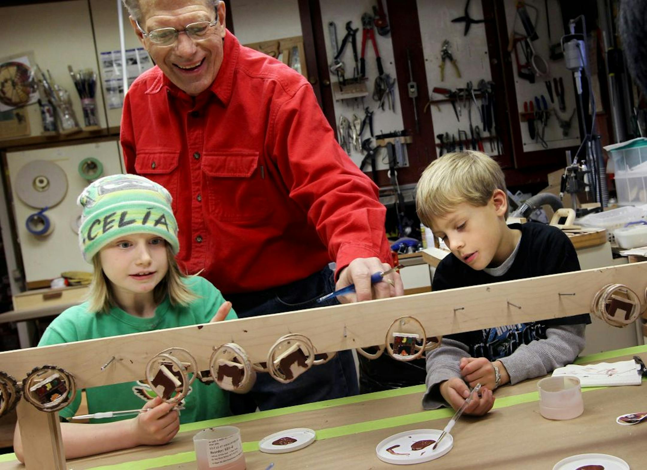 Tom Midtbo, center, touches up some paint applied by grandchildren Celia Midtbo, 8, left, and Sam Skanse, 9, in Tom's basement workshop December 16, 2012. Tom has enlisted his grandchildren as elves to help him make 75 to 100 wooden ornaments every year for friends and family. They are sworn to secrecy until that year's design is presented on Christmas Eve.