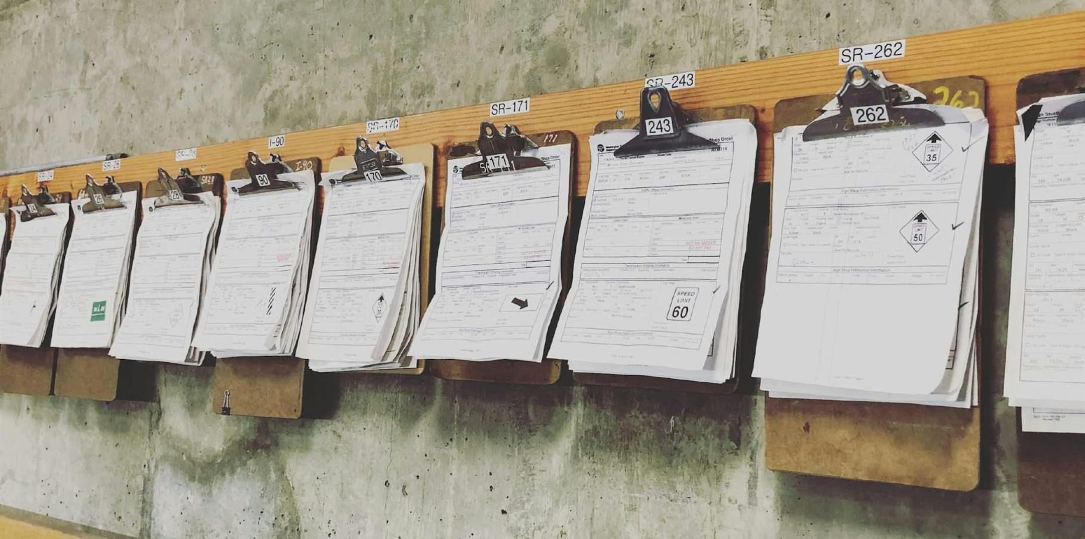 Clipboards with paper inspection sheets hang on the wall of a Washington State Department of Transportation maintenance office in Moses Lake in 2014. The agency's maintenance field staffers now use iPads and apps to inspect everything from guardrails to drainage systems. (Courtesy of the Washington State Department of Transportation)