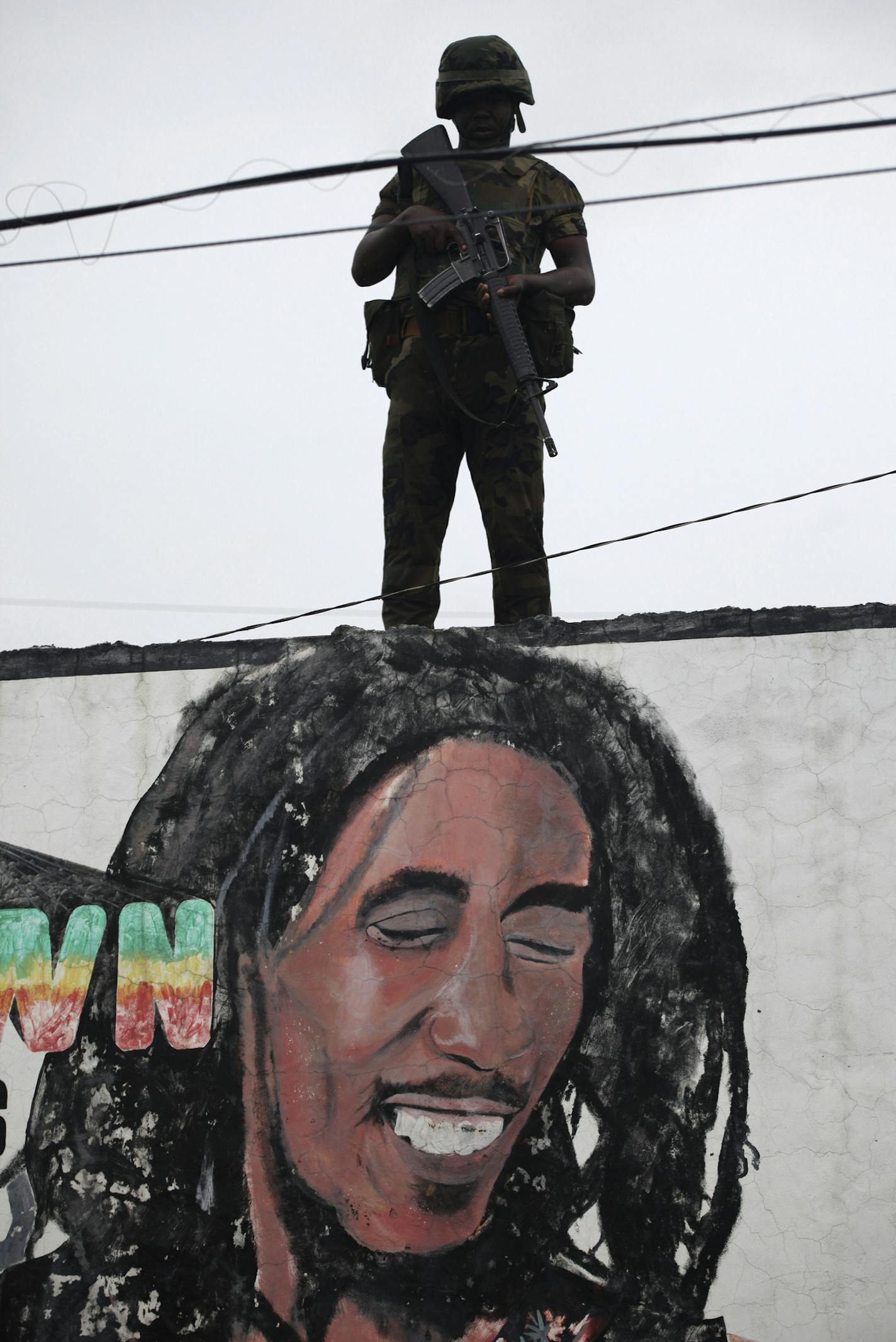 FILE - In this May 28, 2010 file photo, a soldier stands guard above a mural depicting Jamaica's singer-songwriter Bob Marley at a military checkpoint in the crime-ridden Tripoli Gardens neighborhood in Kingston, Jamaica. The Caribbean region, once a leisurely occupation, is facing hard times as an escalating arms race among criminal gangs has turned once-peaceful neighborhoods into battle zones. Jamaica chalked up 1,428 killings in 2010 and St. Kitts and Nevis, a two-island federation of nearly